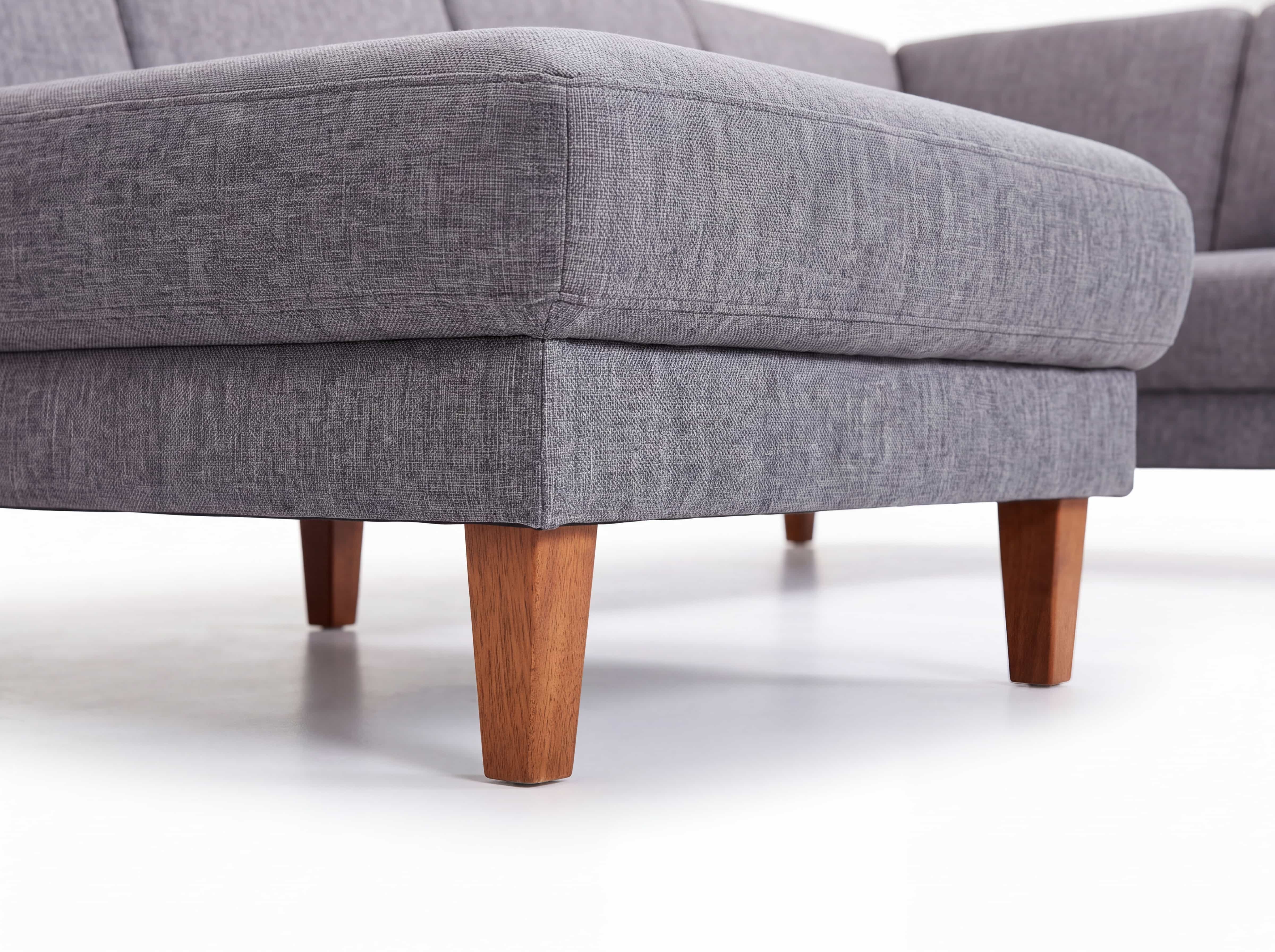 Ecksofa mit grauem Stoffbezug und konisch zulaufenden Holzfüßen, sichtbare Polsterung