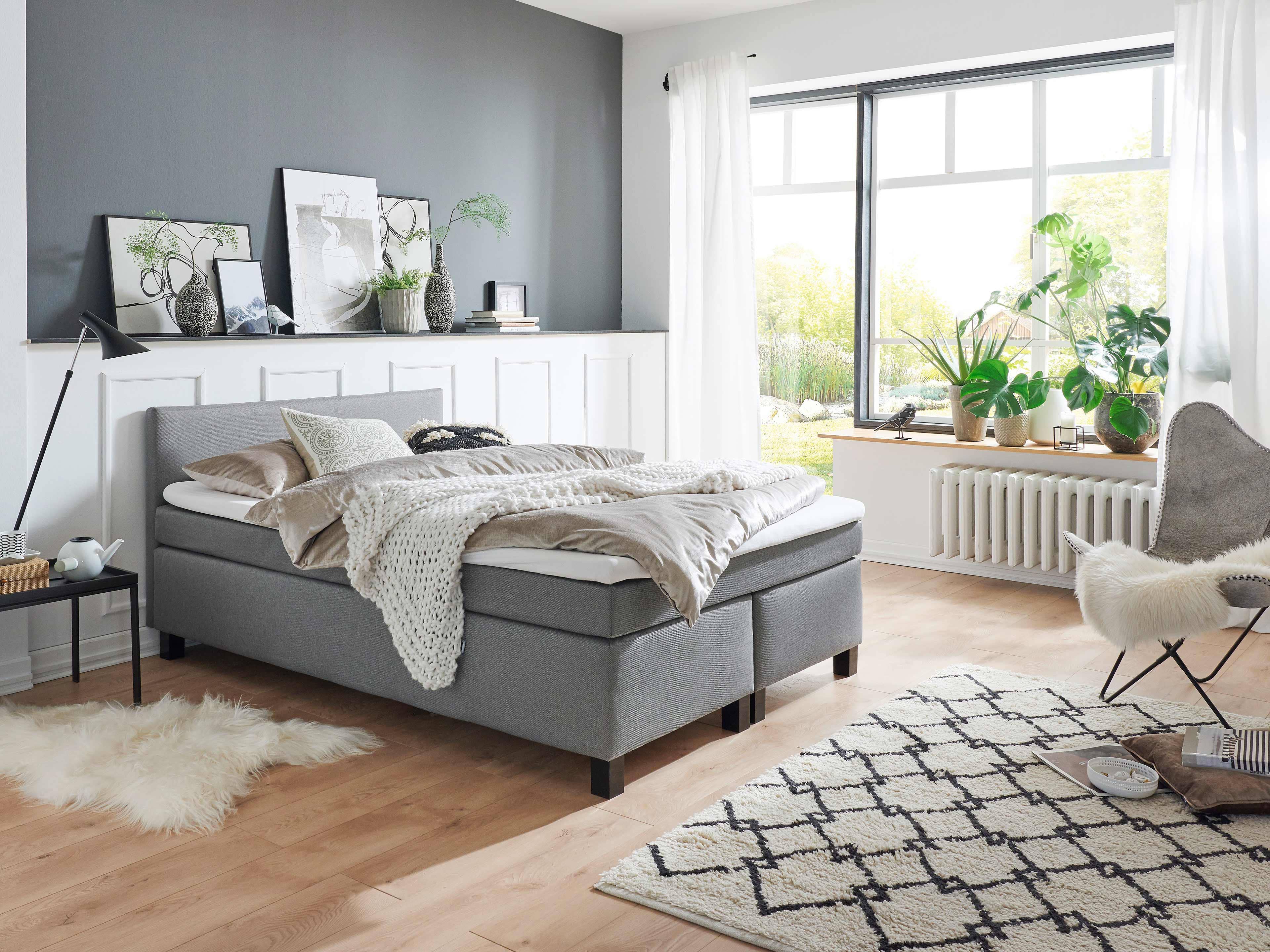 Boxspringbett mit grauem Stoffbezug, rechteckigem gepolstertem Kopfteil und schwarzen Bettfüßen