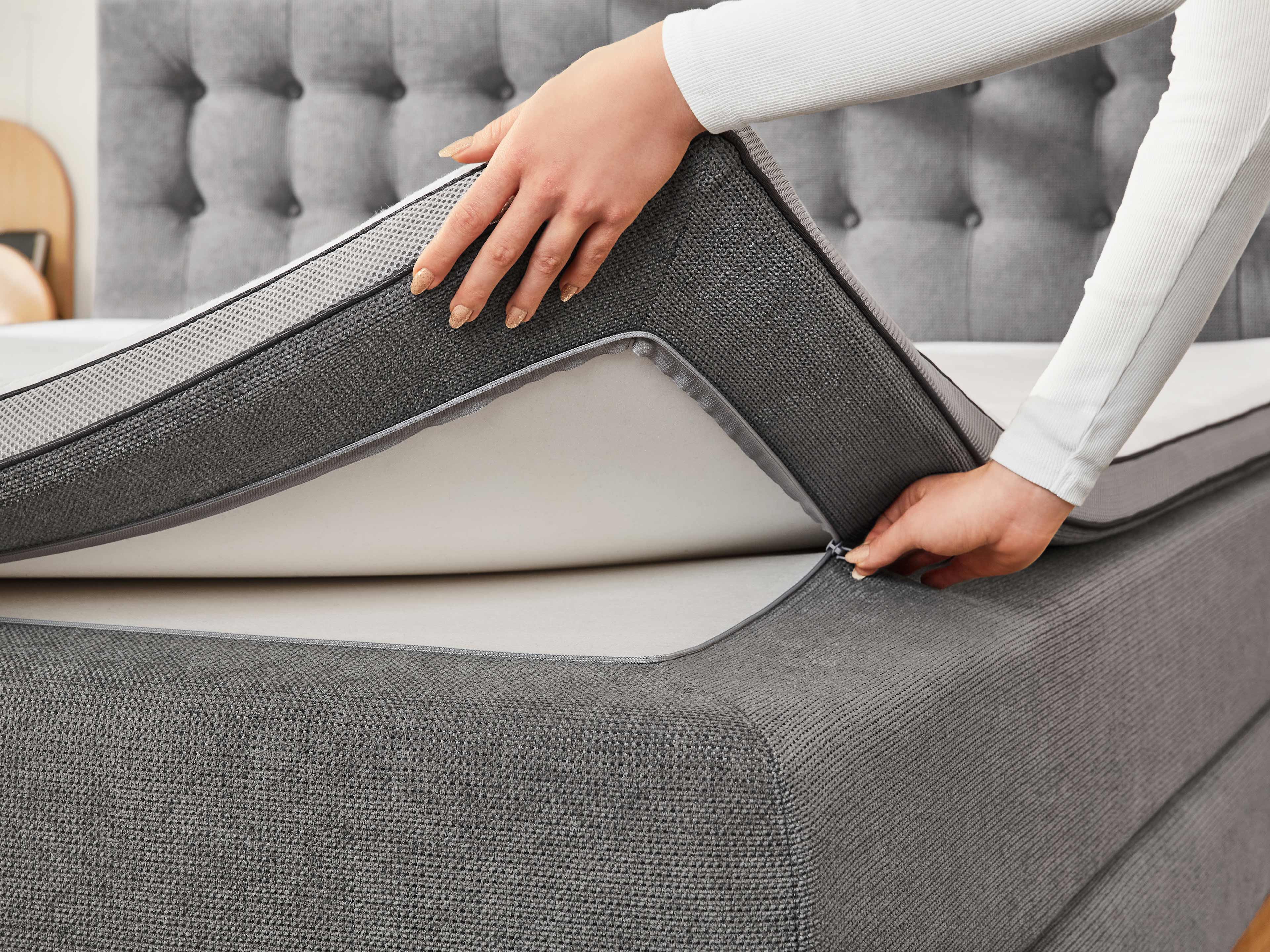 Boxspringbett mit grauem Stoffbezug, gepolstertem Kopfteil und abnehmbarer Matratzenauflage