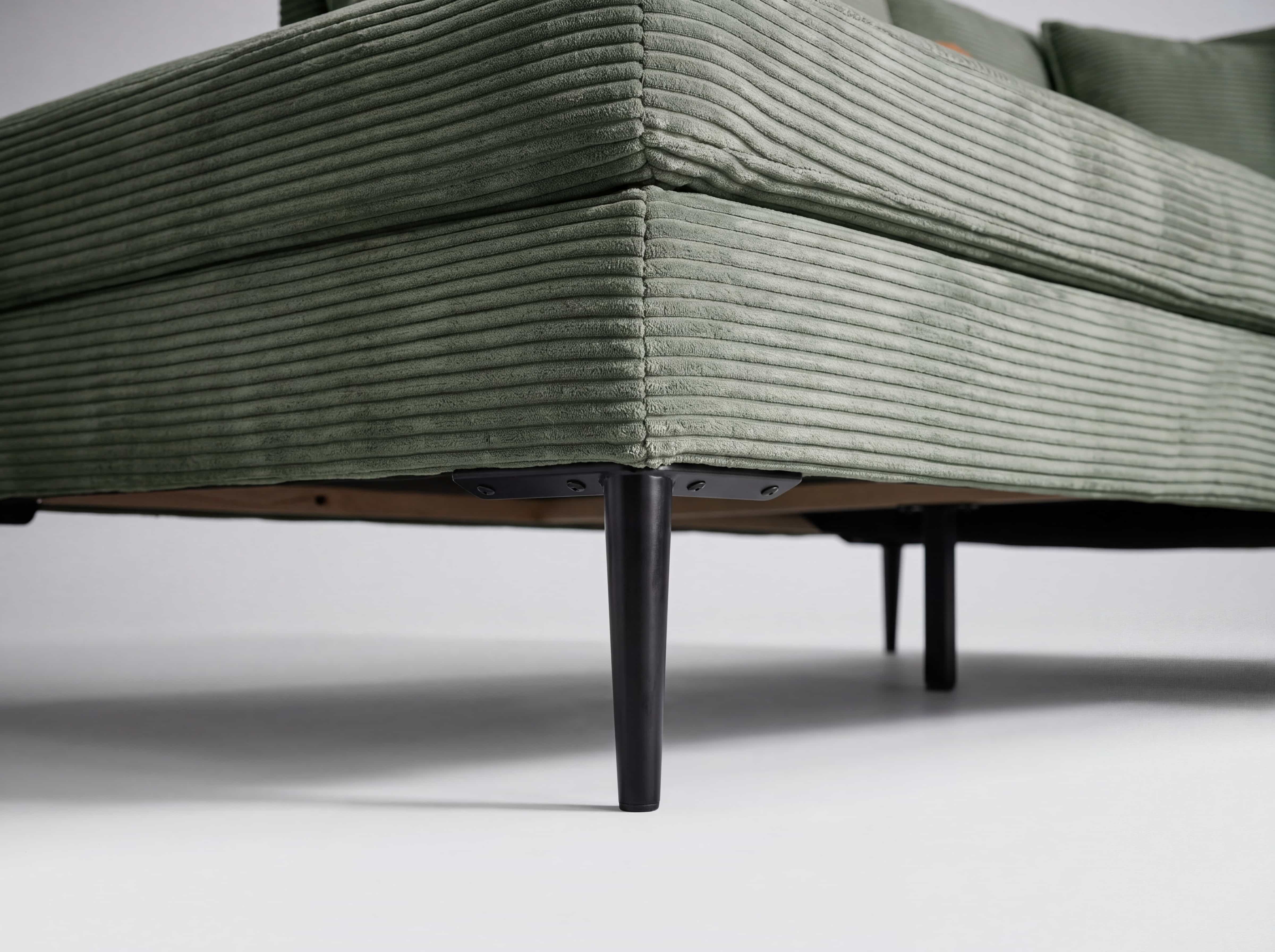 Ecksofa mit grünem Cordbezug, sichtbarem Polstermuster und schwarzen Metallfüßen in Nahaufnahme