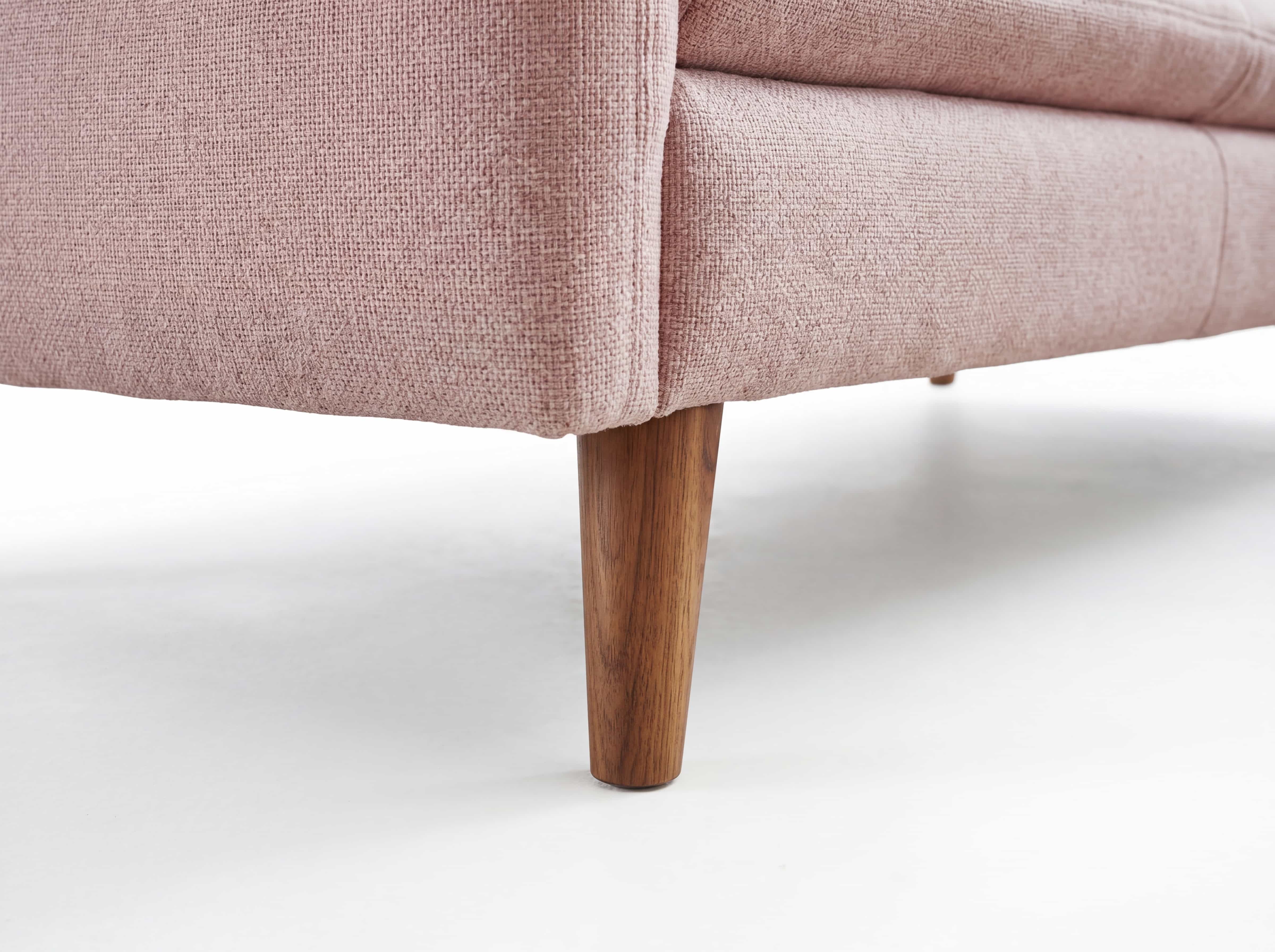 Sofa mit rosa Stoffbezug und konischem Holzfuß, grob strukturierte Oberfläche, Detailansicht