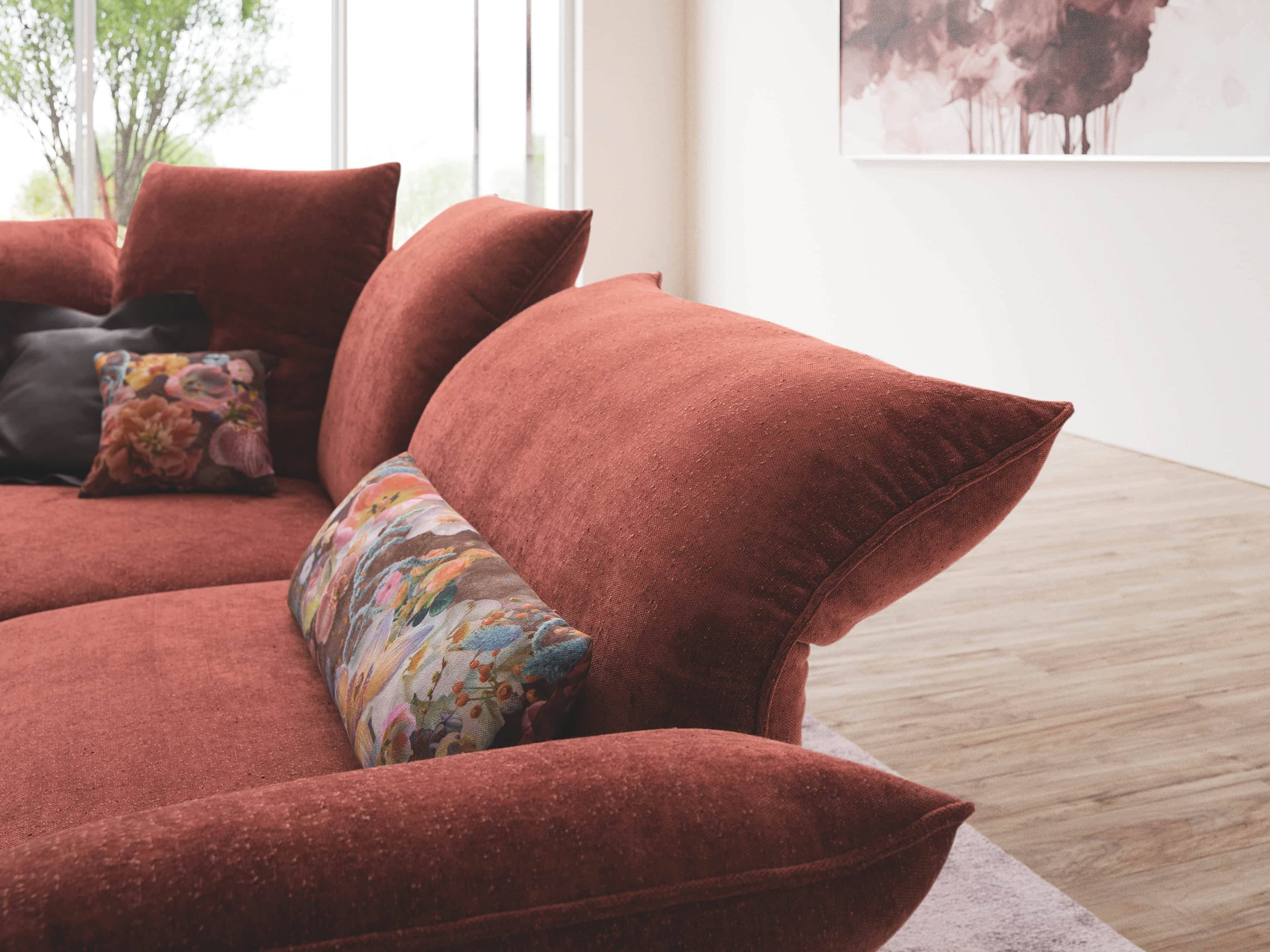 Ecksofa Modellname mit rotem Stoffbezug, großer Rückenlehne und gemusterten Zierkissen