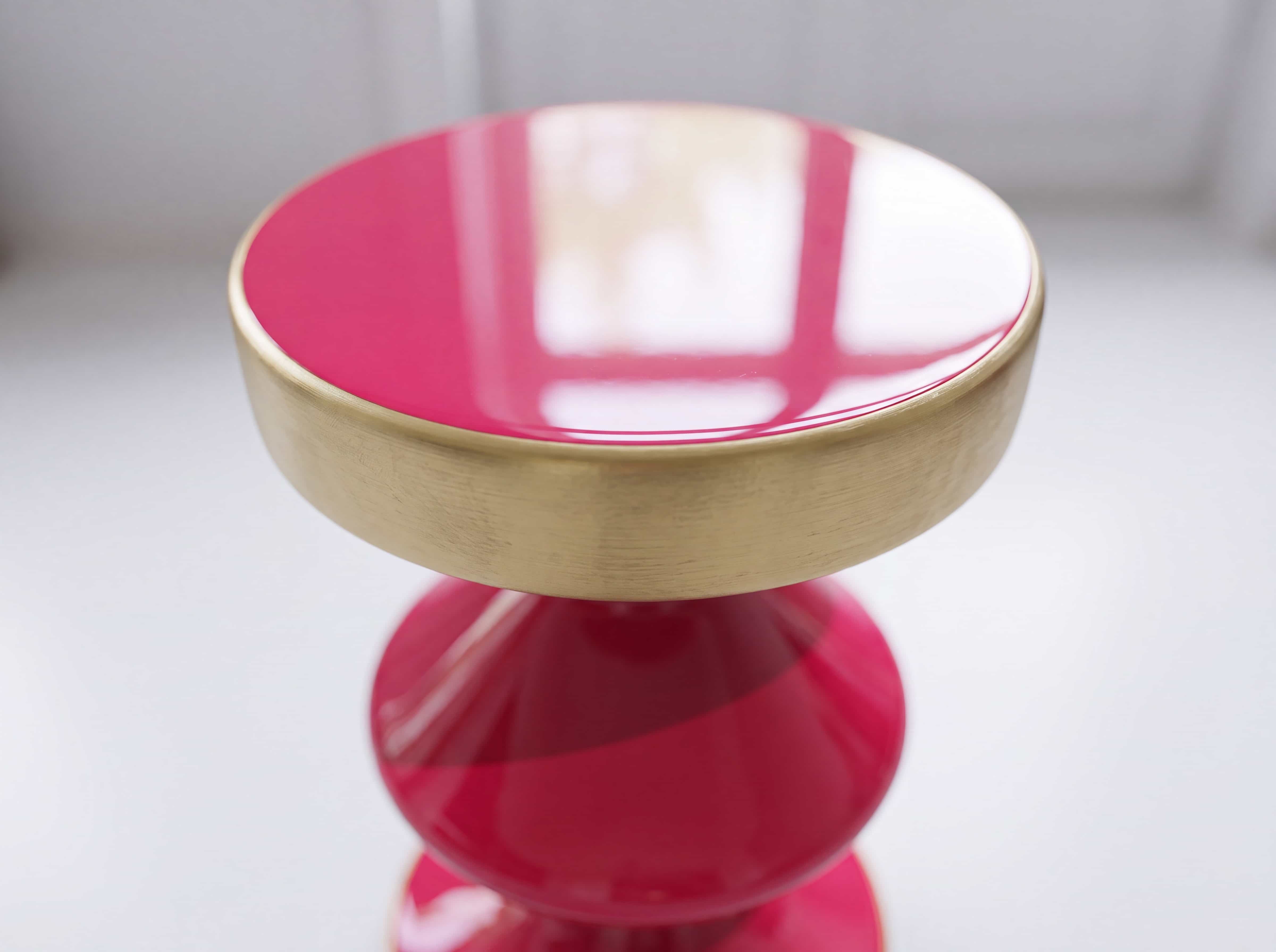 Runder Beistelltisch mit glänzender pinker Platte und goldenem Rand, Sockel in Pink gehalten.