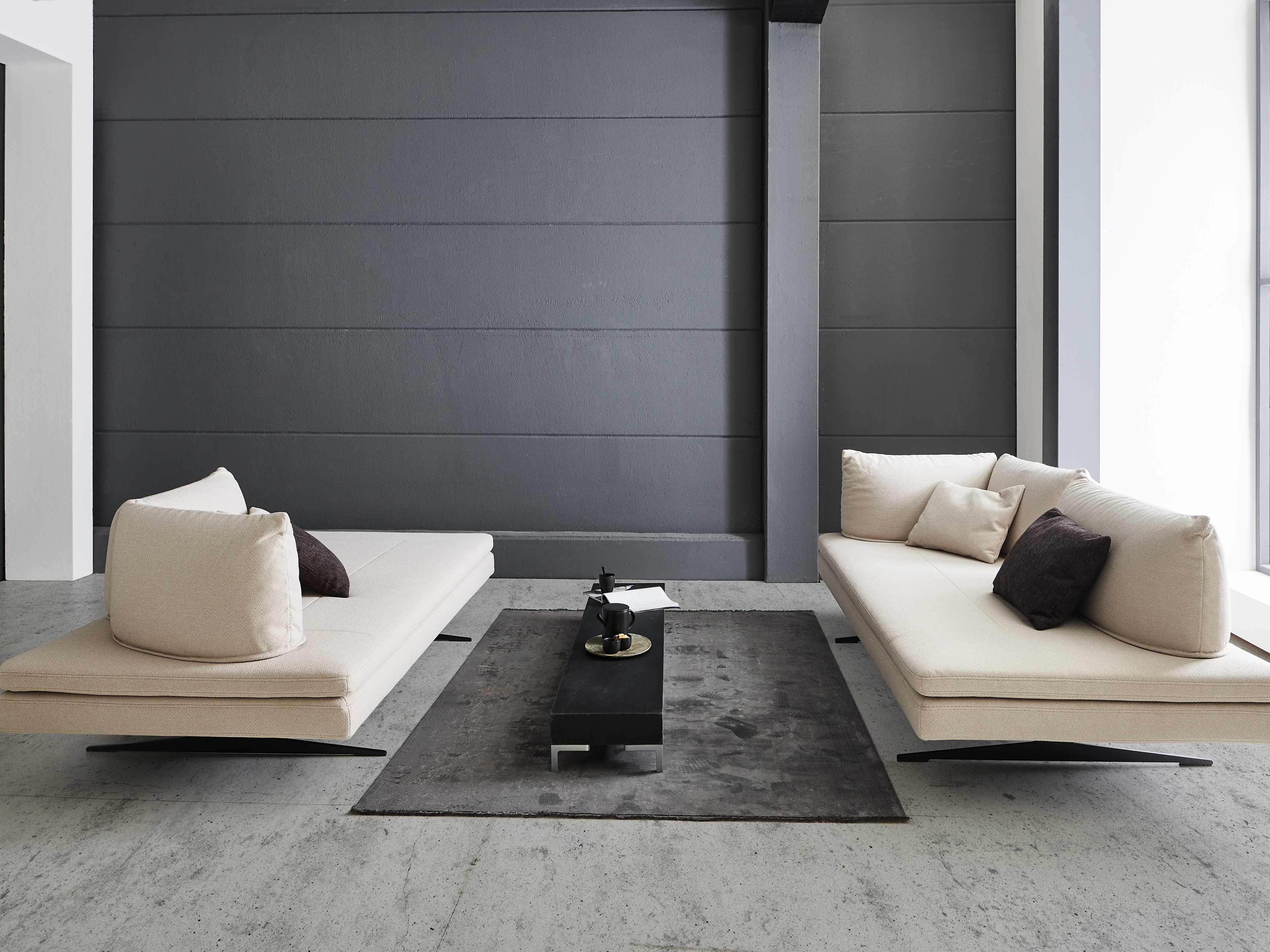 Modernes 2-Sitzer Sofa mit beigem Stoffbezug, niedriger Rückenlehne und schwarzen Standfüßen.