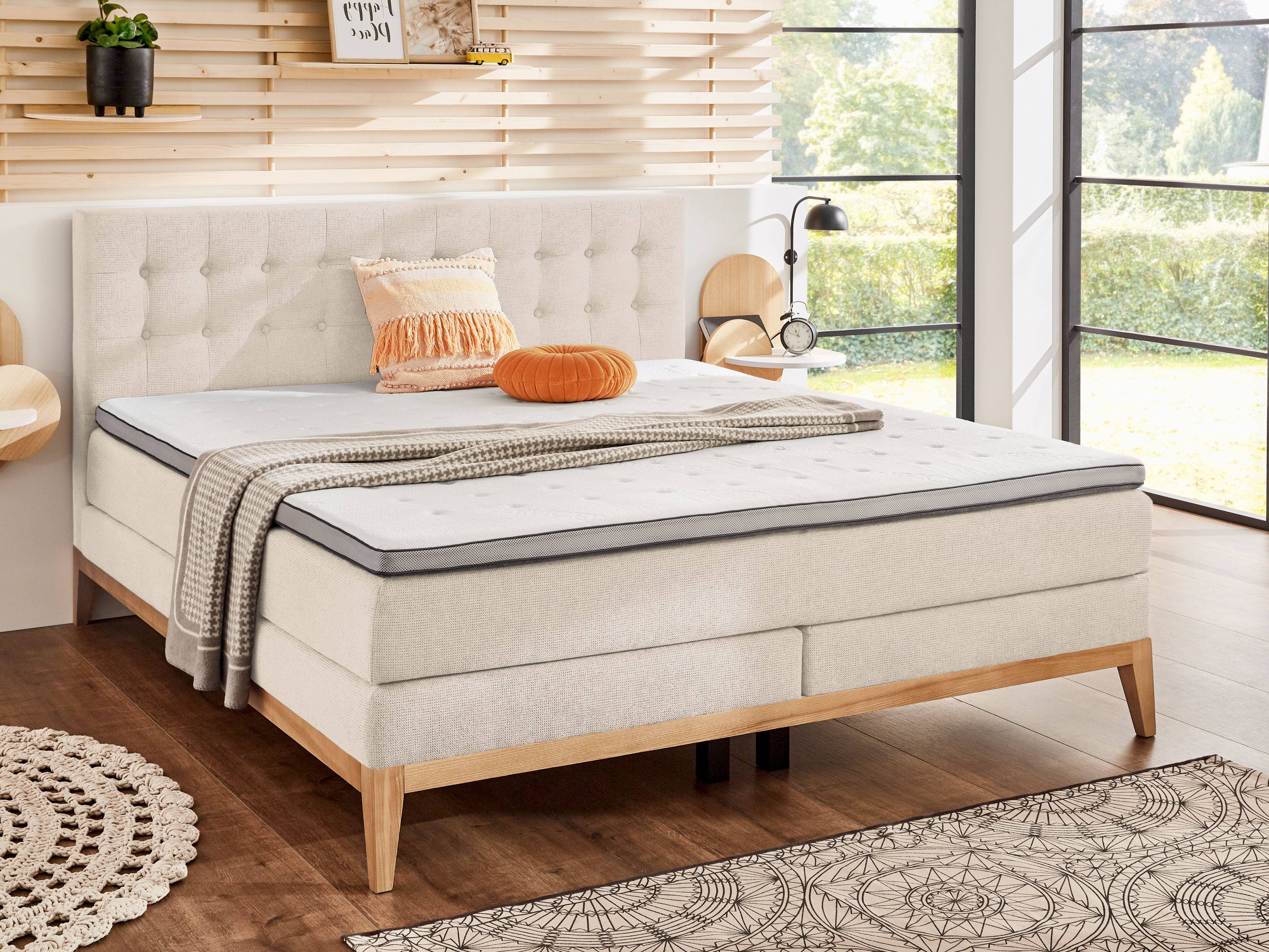 Boxspringbett mit hellem Stoffbezug, gepolstertem Kopfteil mit Knopfheftung und Holzfüßen