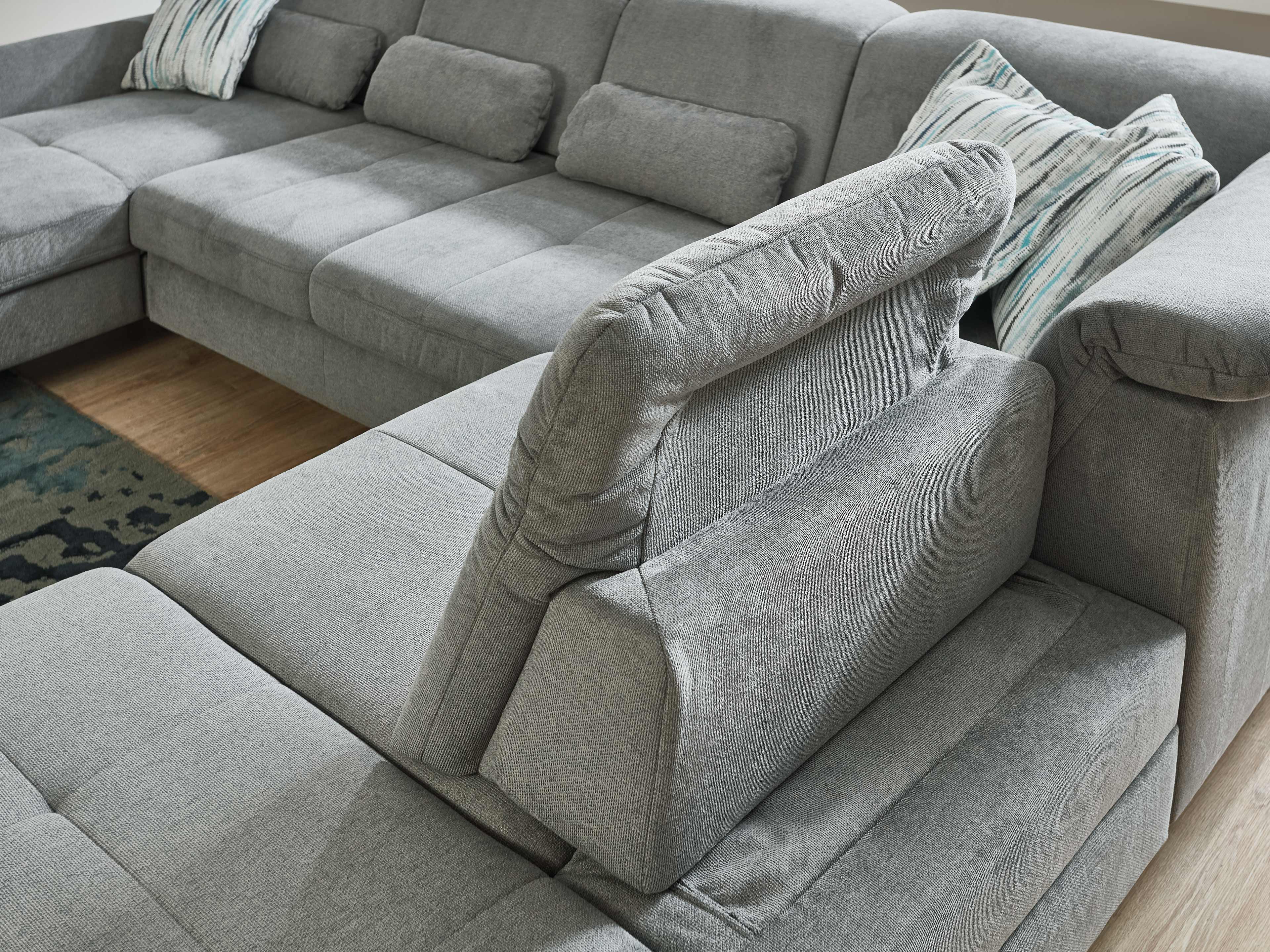 Ecksofa mit grauem Stoffbezug, verstellbarer Rückenlehne, Armlehnen und mehreren Kissen.