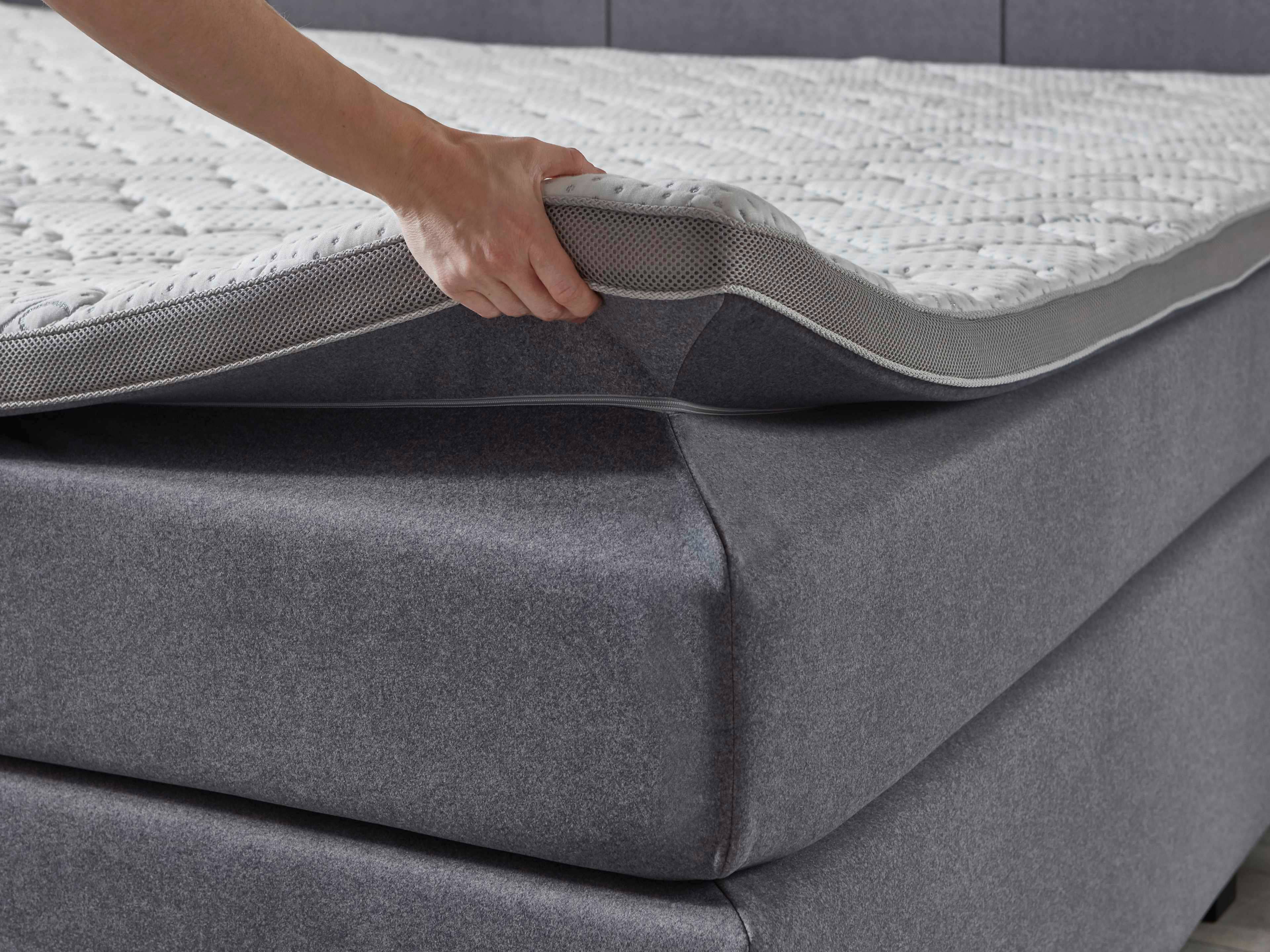 Boxspringbett mit grauem Stoffbezug und sichtbarem Topper, Detailansicht der Matratzenauflage