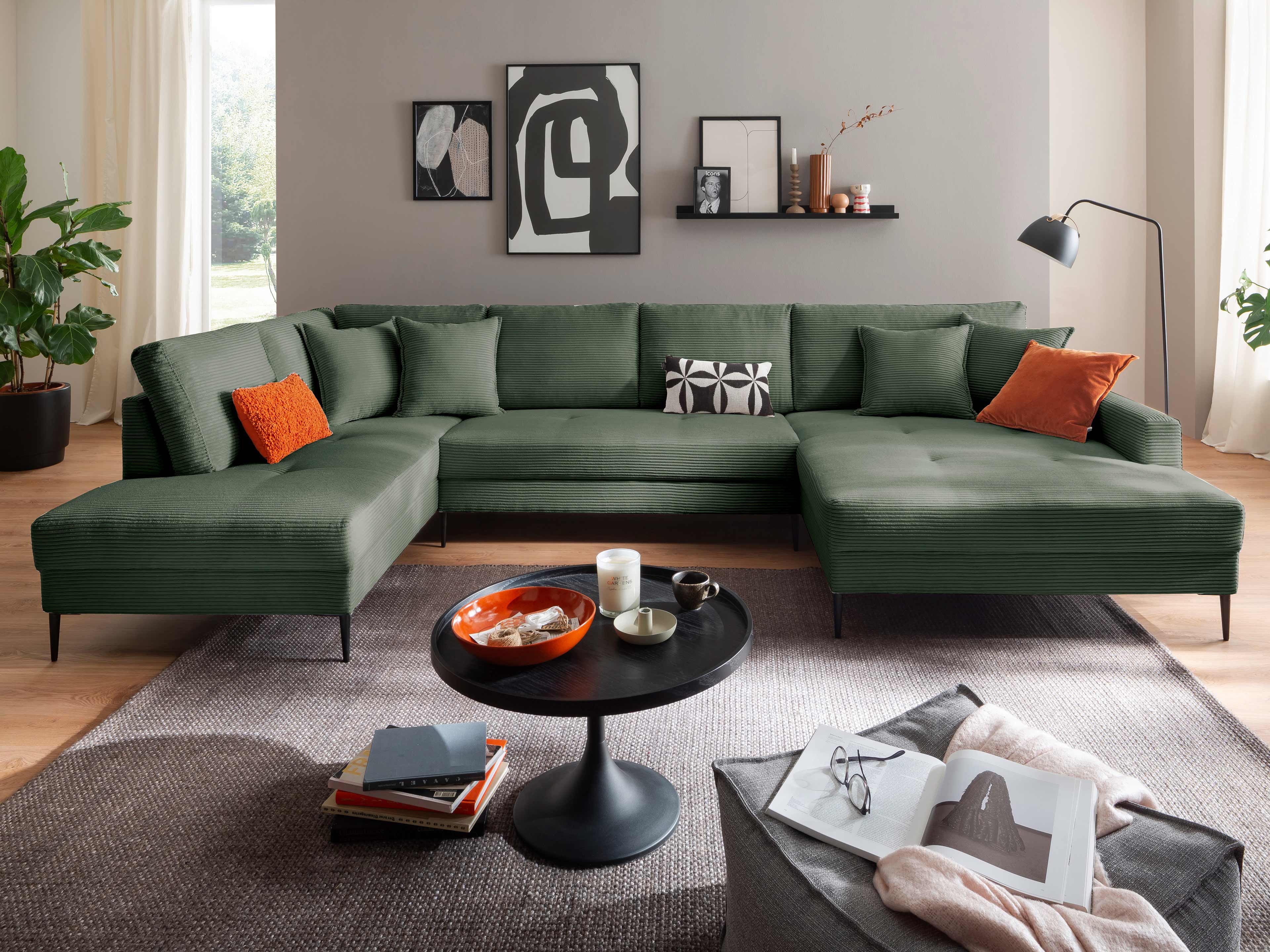 Ecksofa Kabs Polsterwelt mit grünem Cordbezug, L-Form, schwarzen Füßen und mehreren Kissen.