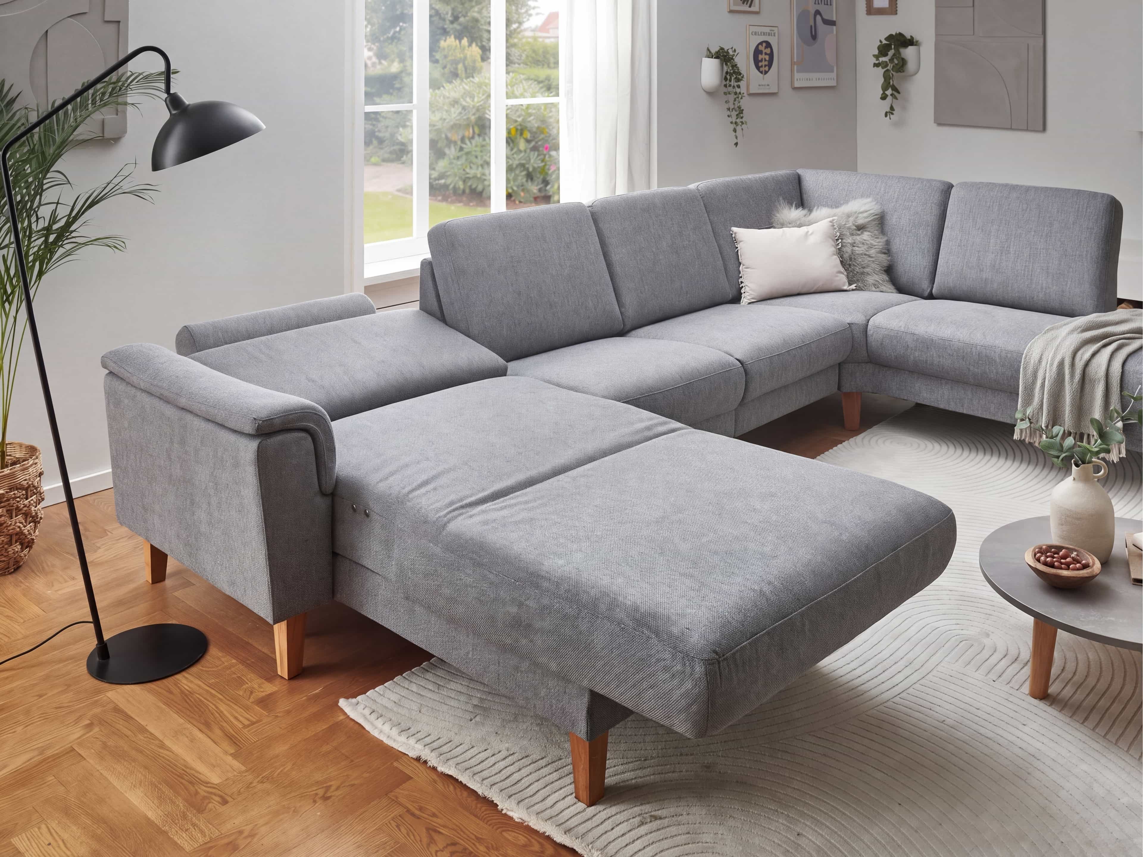 Ecksofa Kabs mit grauem Stoffbezug, Schlaffunktion, Armlehnen und Holzfüßen, gepolstert
