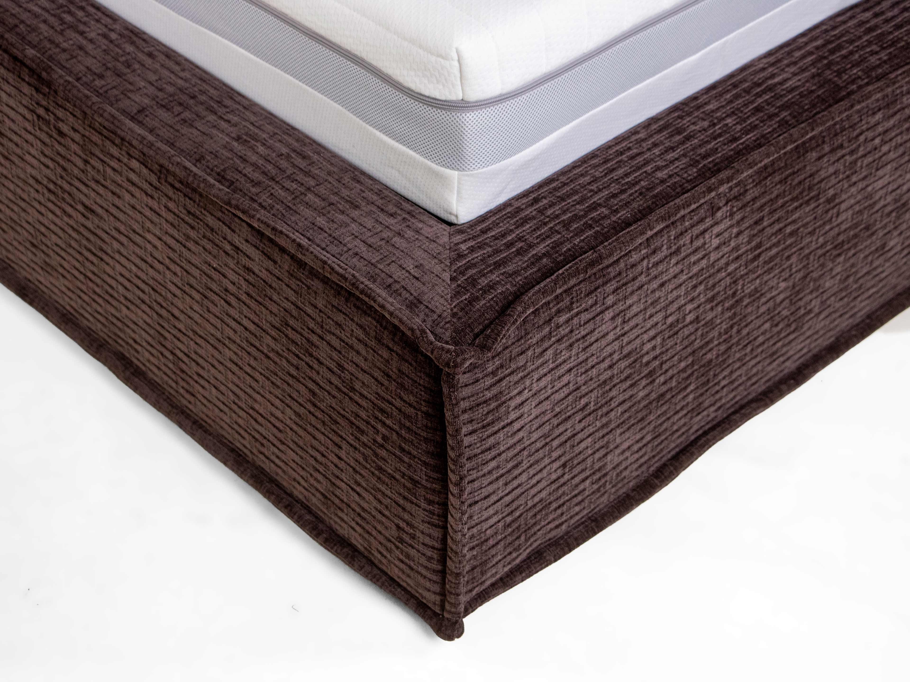Boxspringbett mit hellgrauer Matratze und strukturiertem, dunkelbraunem Stoffbezug am Unterbau