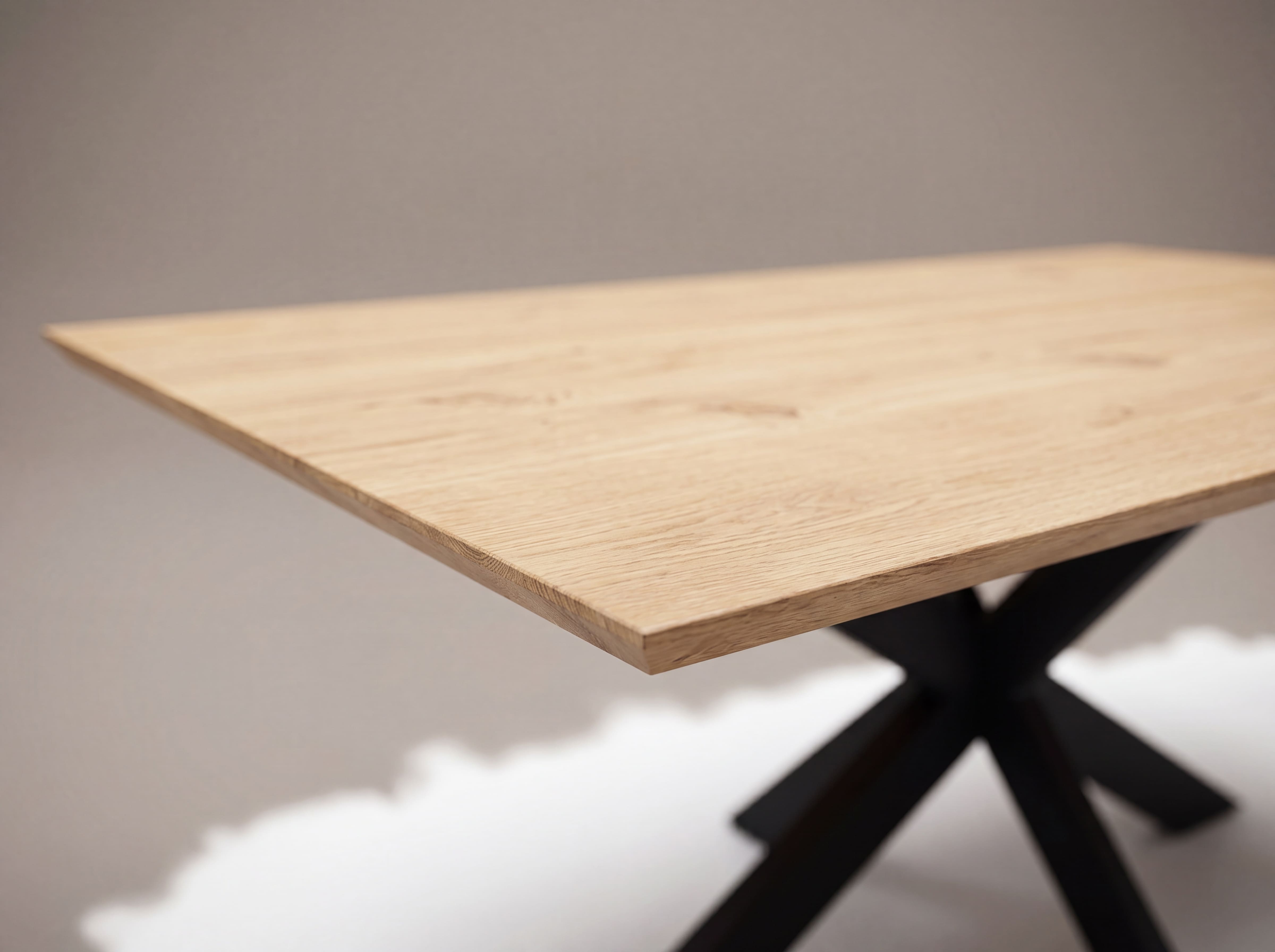 Esstisch mit rechteckiger Tischplatte aus hellem Holz und schwarzem Kreuzgestell, Detailansicht.