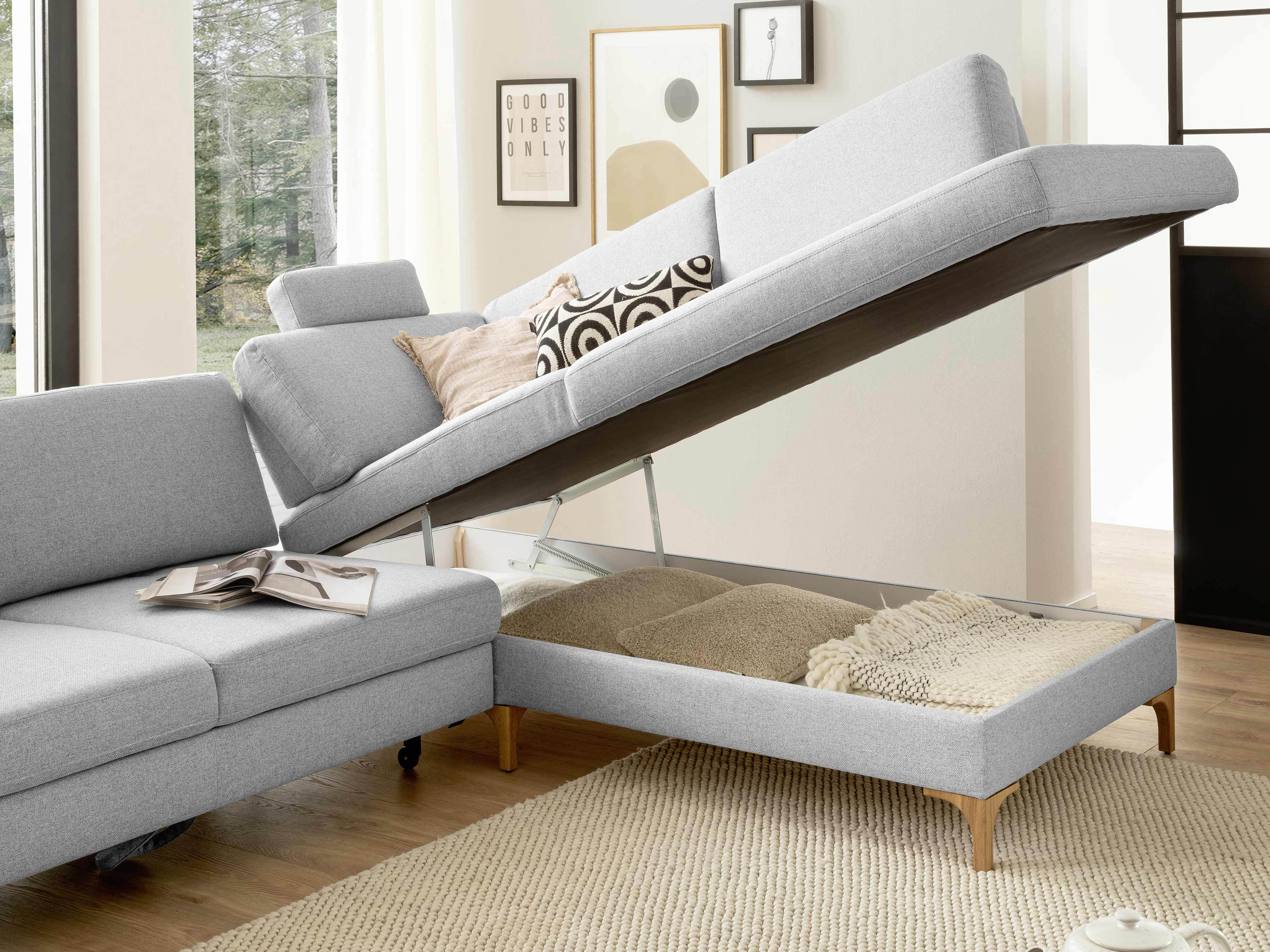 Ecksofa mit hellgrauem Stoffbezug, Holzfüßen und aufklappbarer Sitzfläche mit Stauraumfunktion