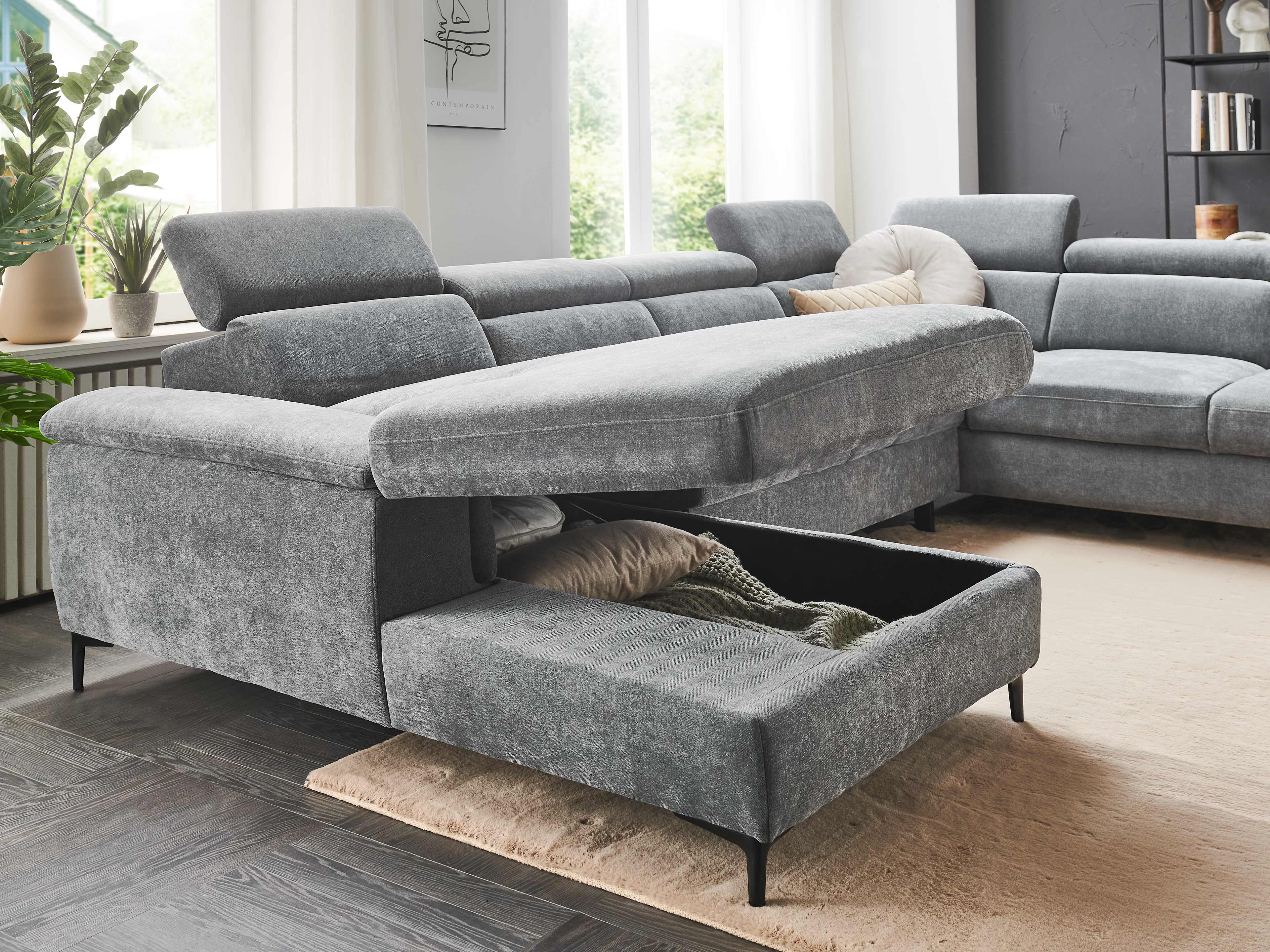 Ecksofa Modell mit grauem Stoffbezug, verstellbaren Kopfteilen und offenem Bettkasten auf schwarzen Füßen