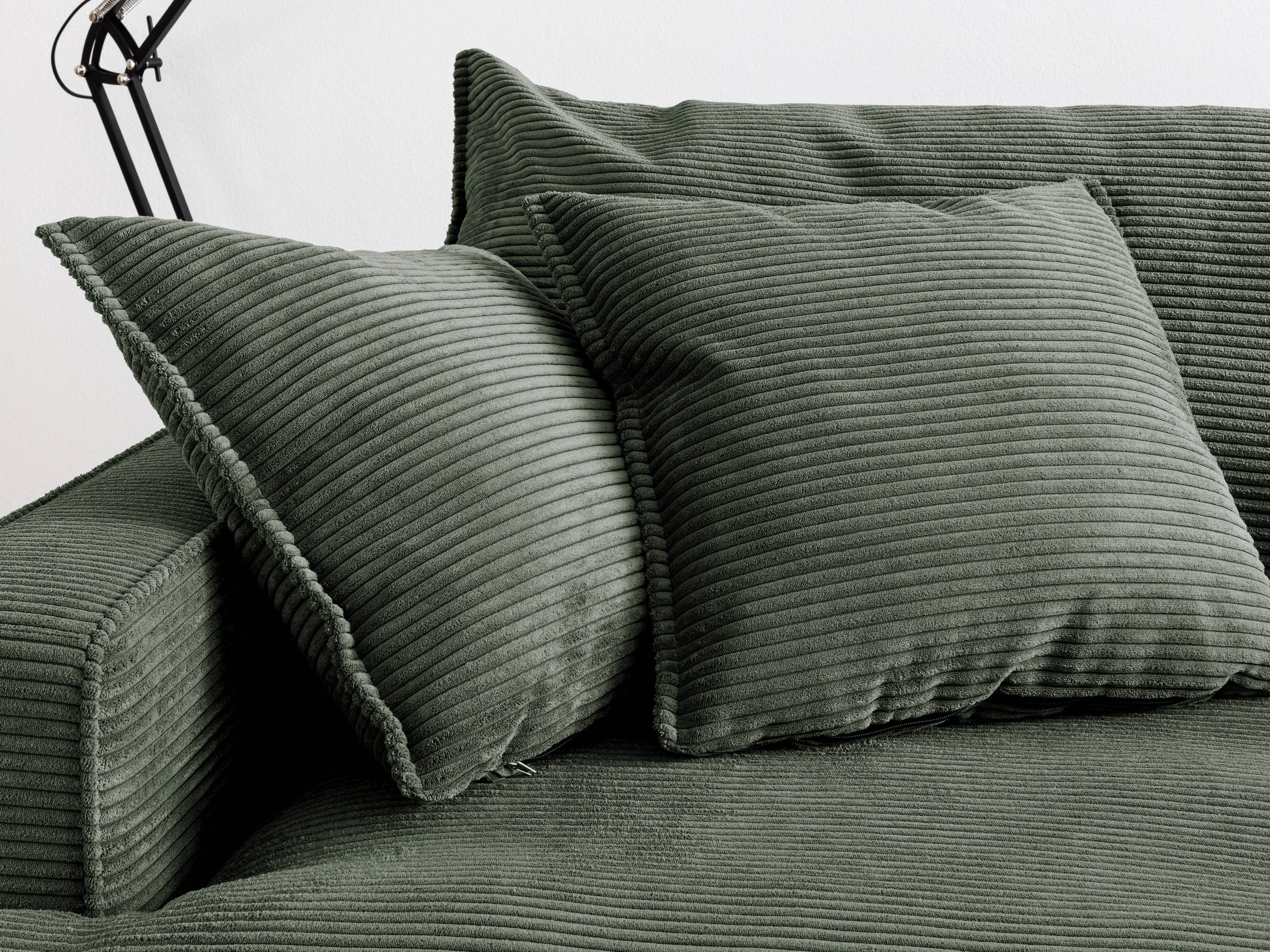 Zwei quadratische Dekokissen aus grünem Cordstoff mit markantem Rippenmuster auf Sofa.