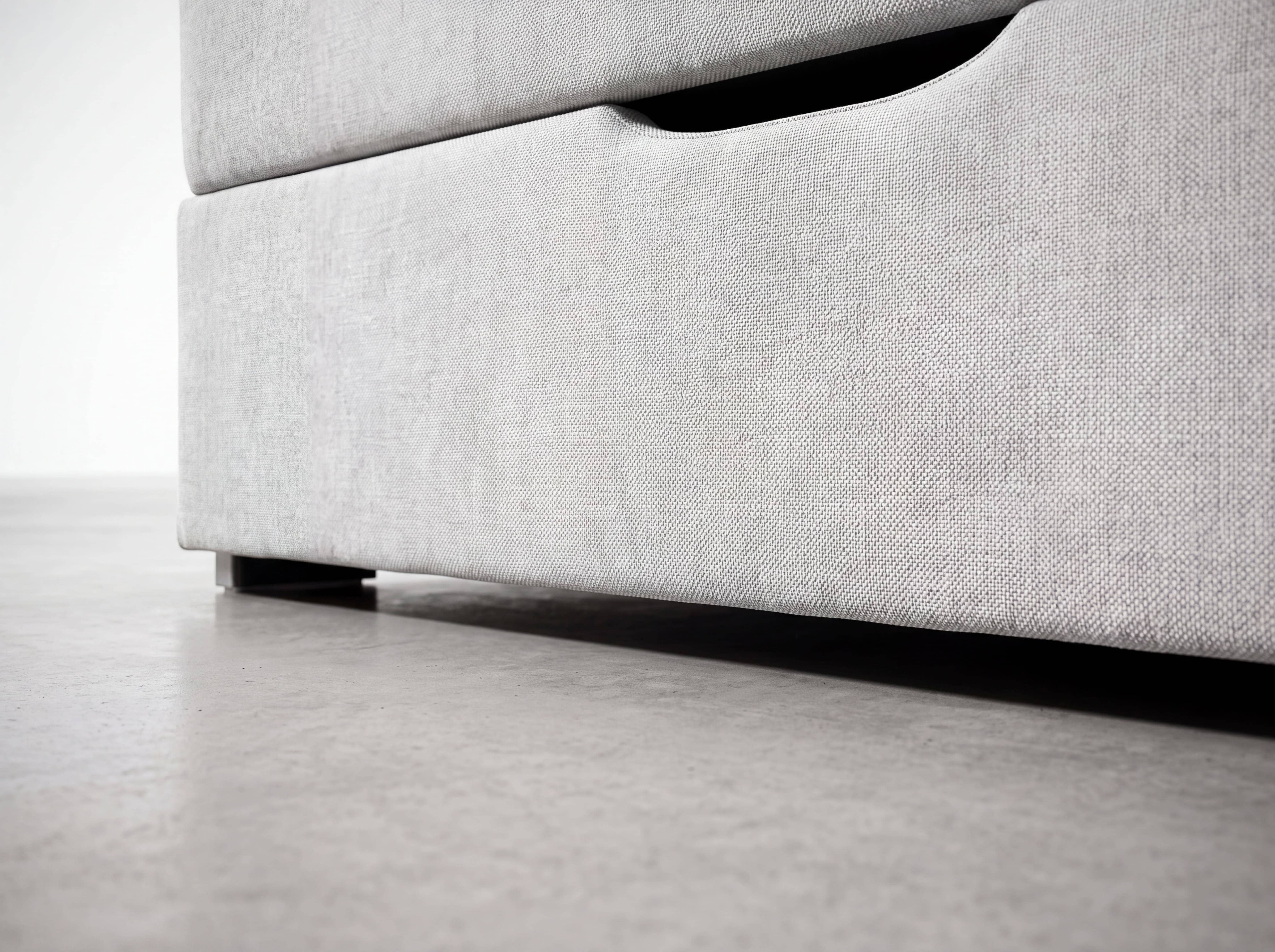 Boxspringbett mit hellgrauem Stoffbezug, sichtbarem Bettkasten und Aussparung als Griffmulde