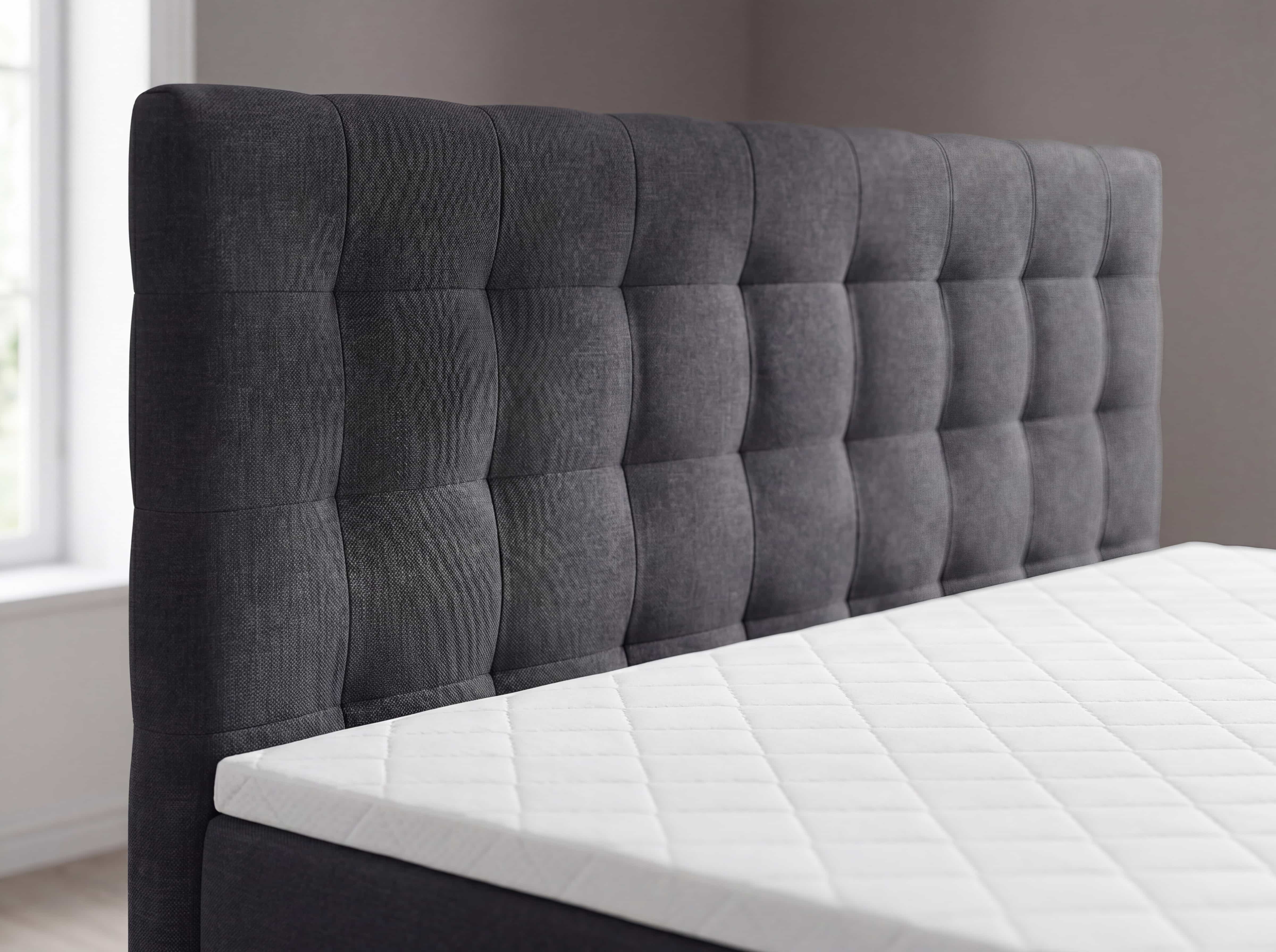 Boxspringbett mit grauem Stoffbezug, gepolstertem Kopfteil und markanter Rechteck-Steppung