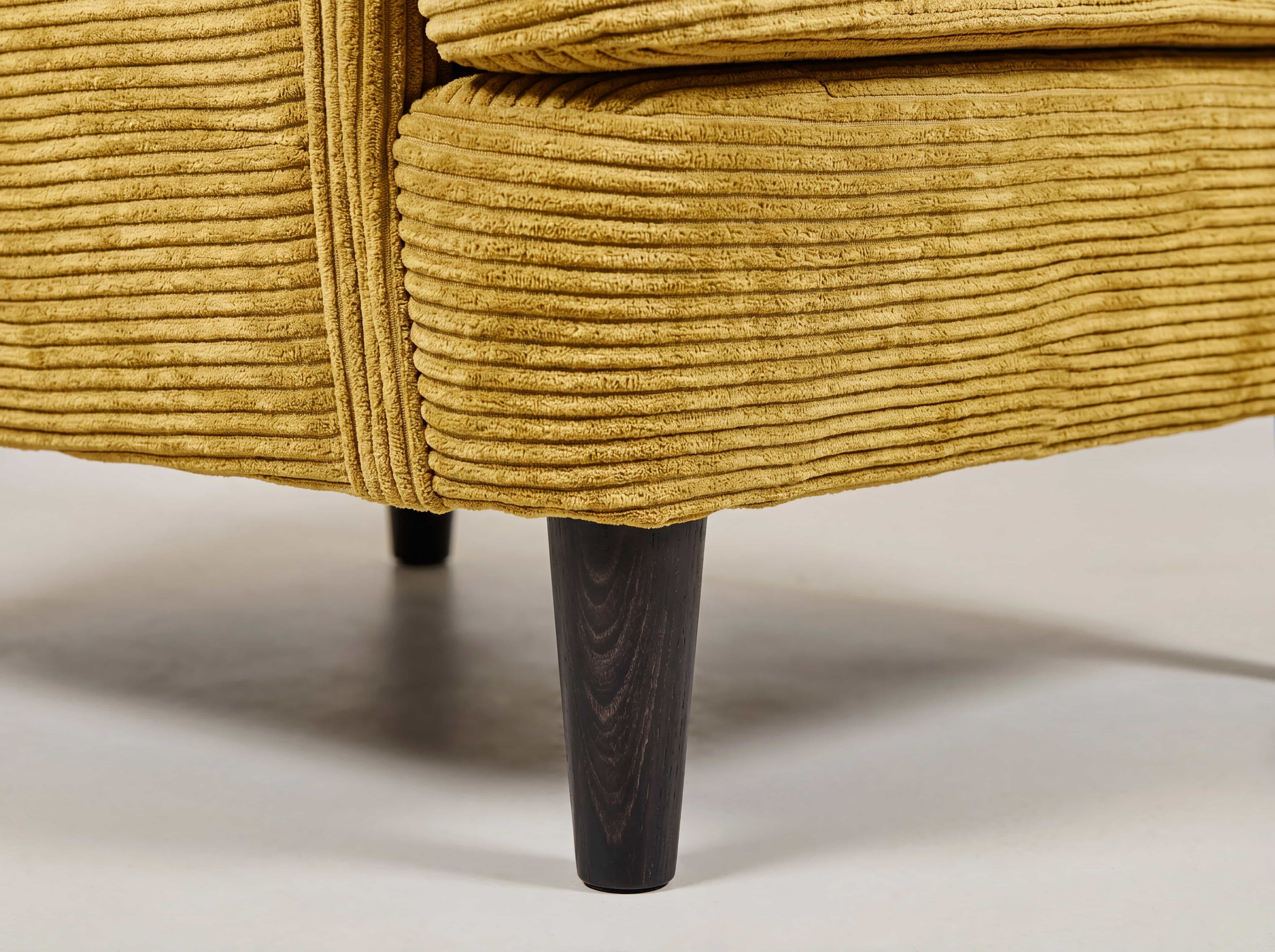 Detailansicht eines Sofas mit gelbem Cordbezug und konischem Bein aus dunklem Holz.