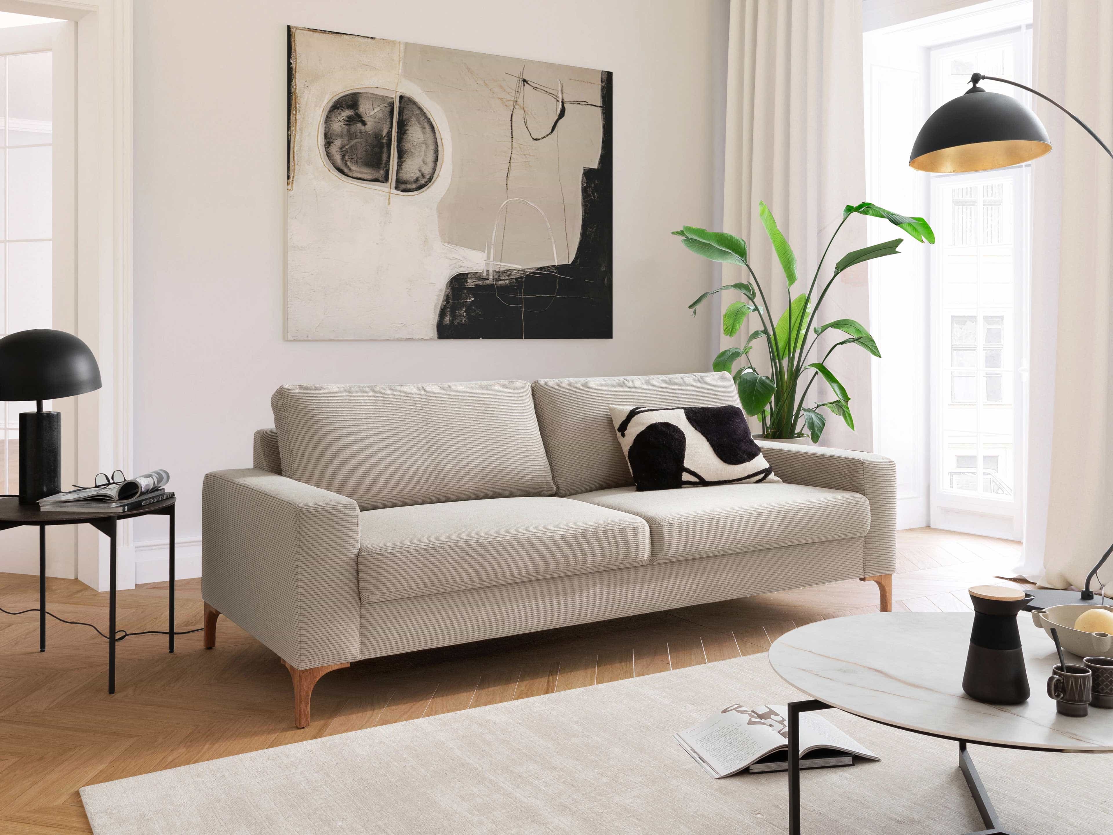 3-Sitzer Sofa Kabs Polsterwelt mit hellbeigem Stoffbezug, Armlehnen und sichtbaren Holzfüßen
