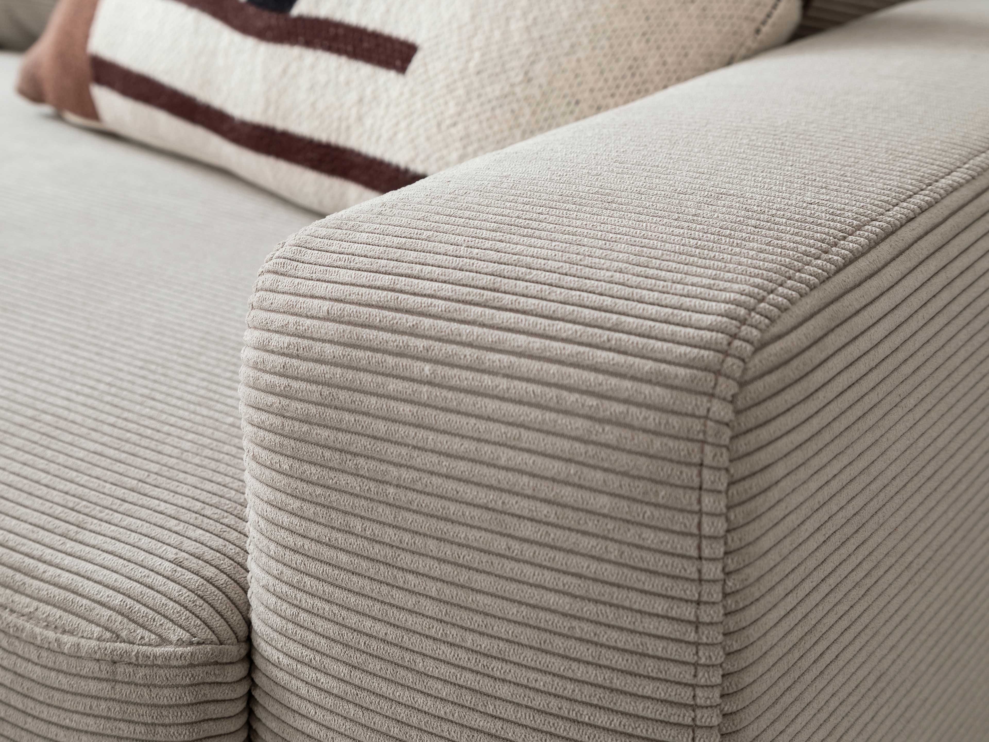 Detailaufnahme eines beigen Sofas mit breiter Armlehne und sichtbarer Cordstruktur im Stoffbezug