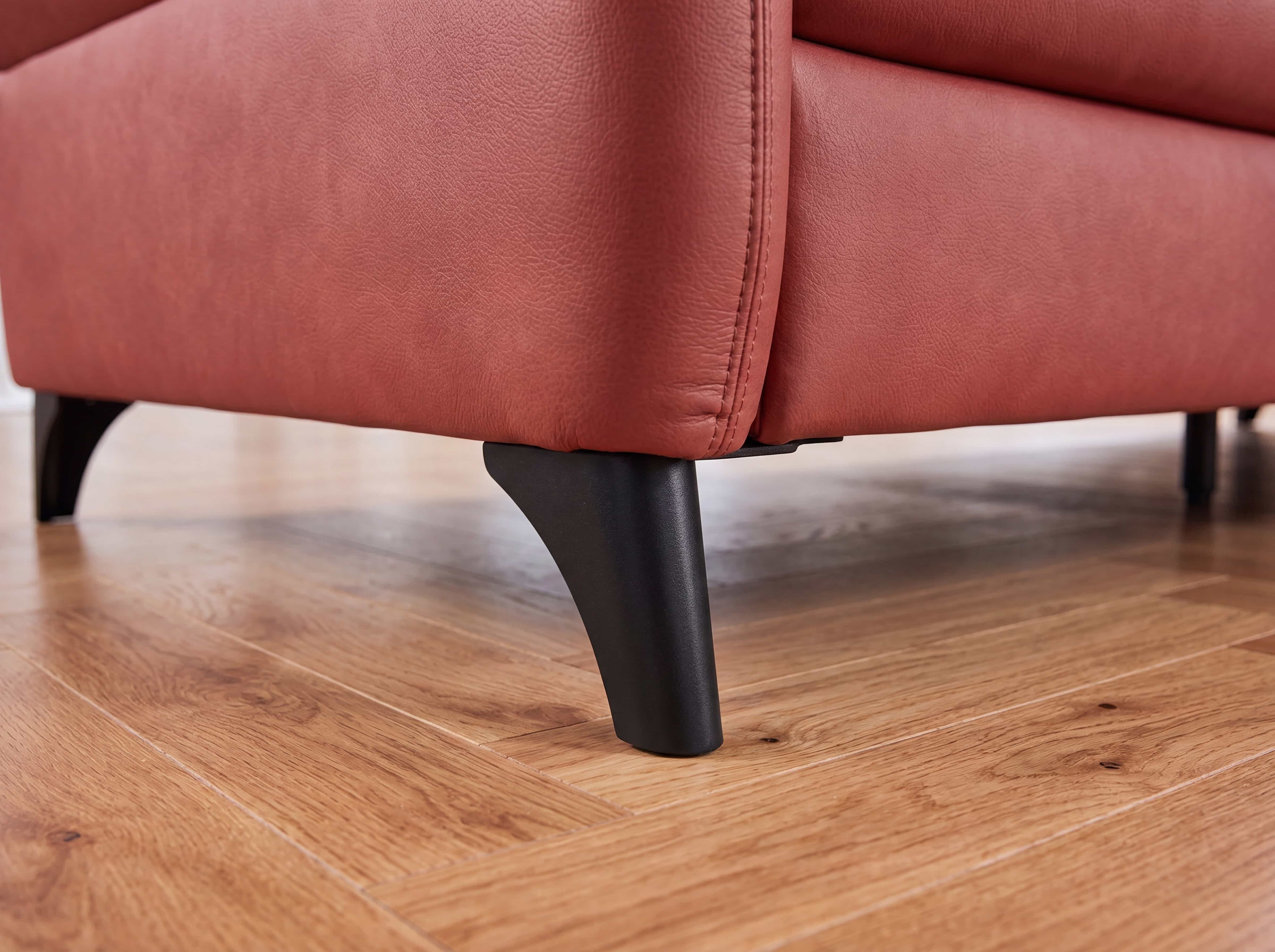 Sofa mit rosafarbenem Lederbezug und schwarzen, konisch geformten Füßen auf Holzfußboden