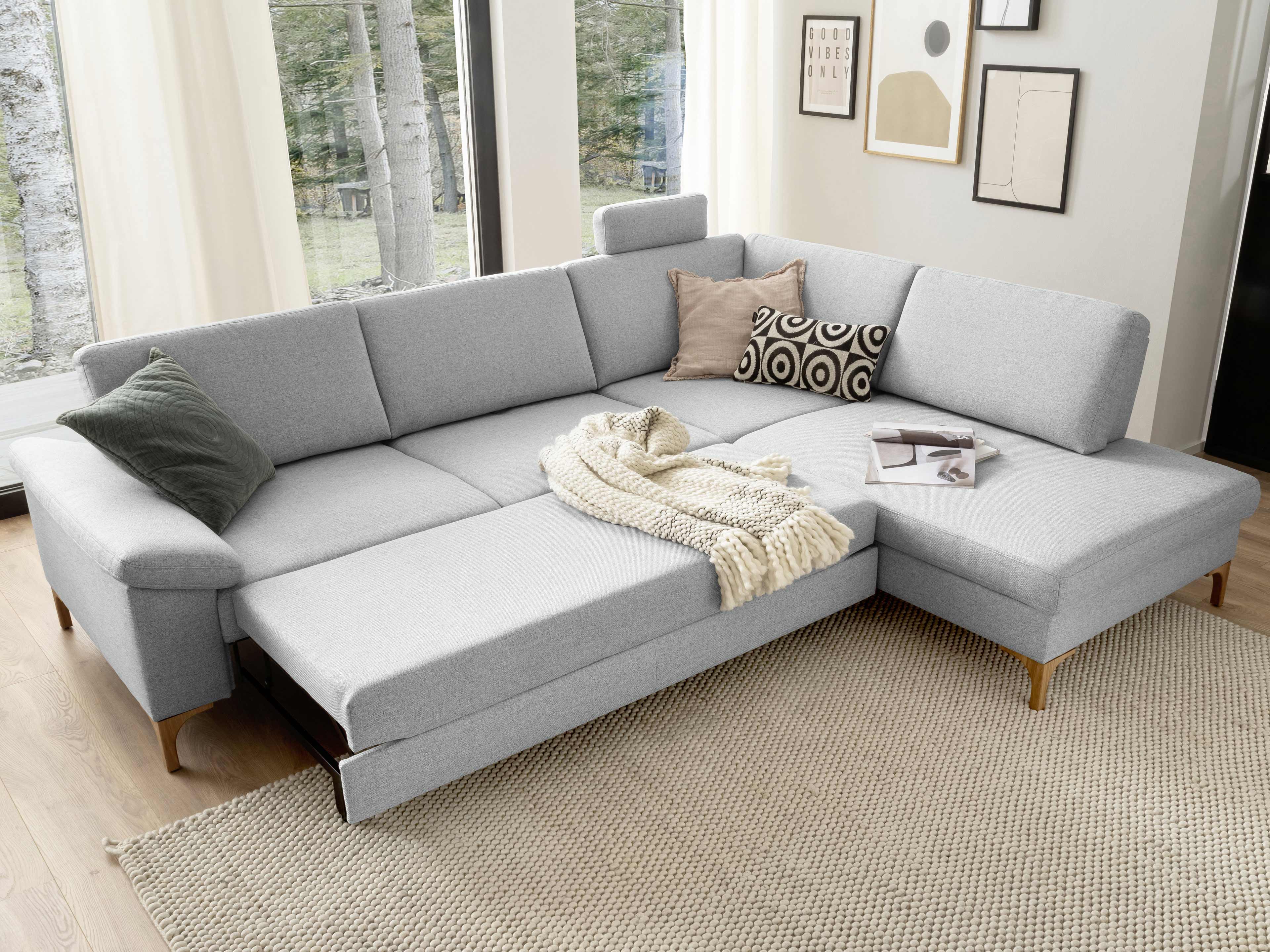 Ecksofa in L-Form mit hellgrauem Stoffbezug, Holzfüßen, Armlehnen und ausziehbarer Liegefläche