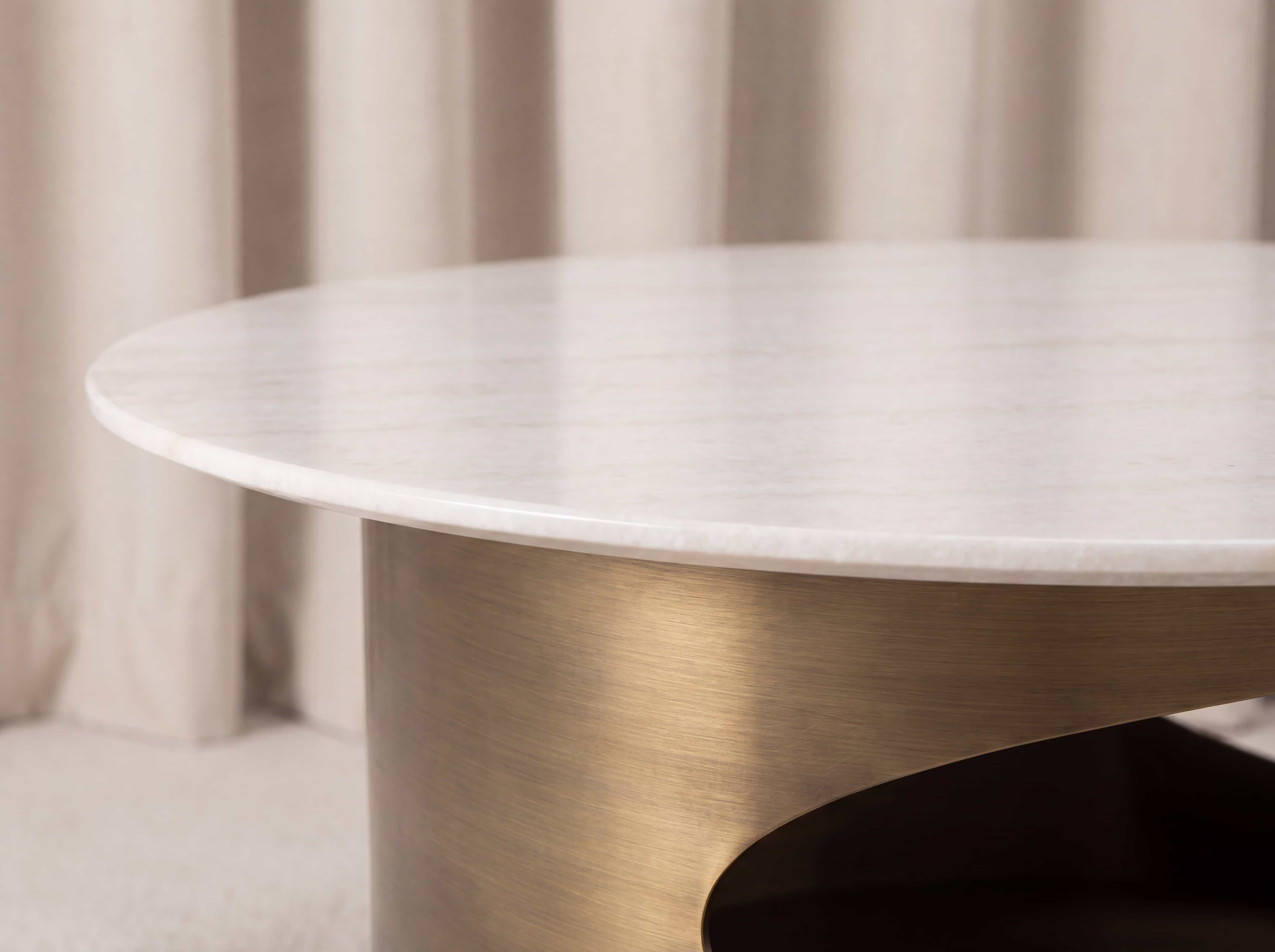 Runder Couchtisch mit weißer Marmorplatte und gebogenem, goldfarbenem Metallgestell im Detail.