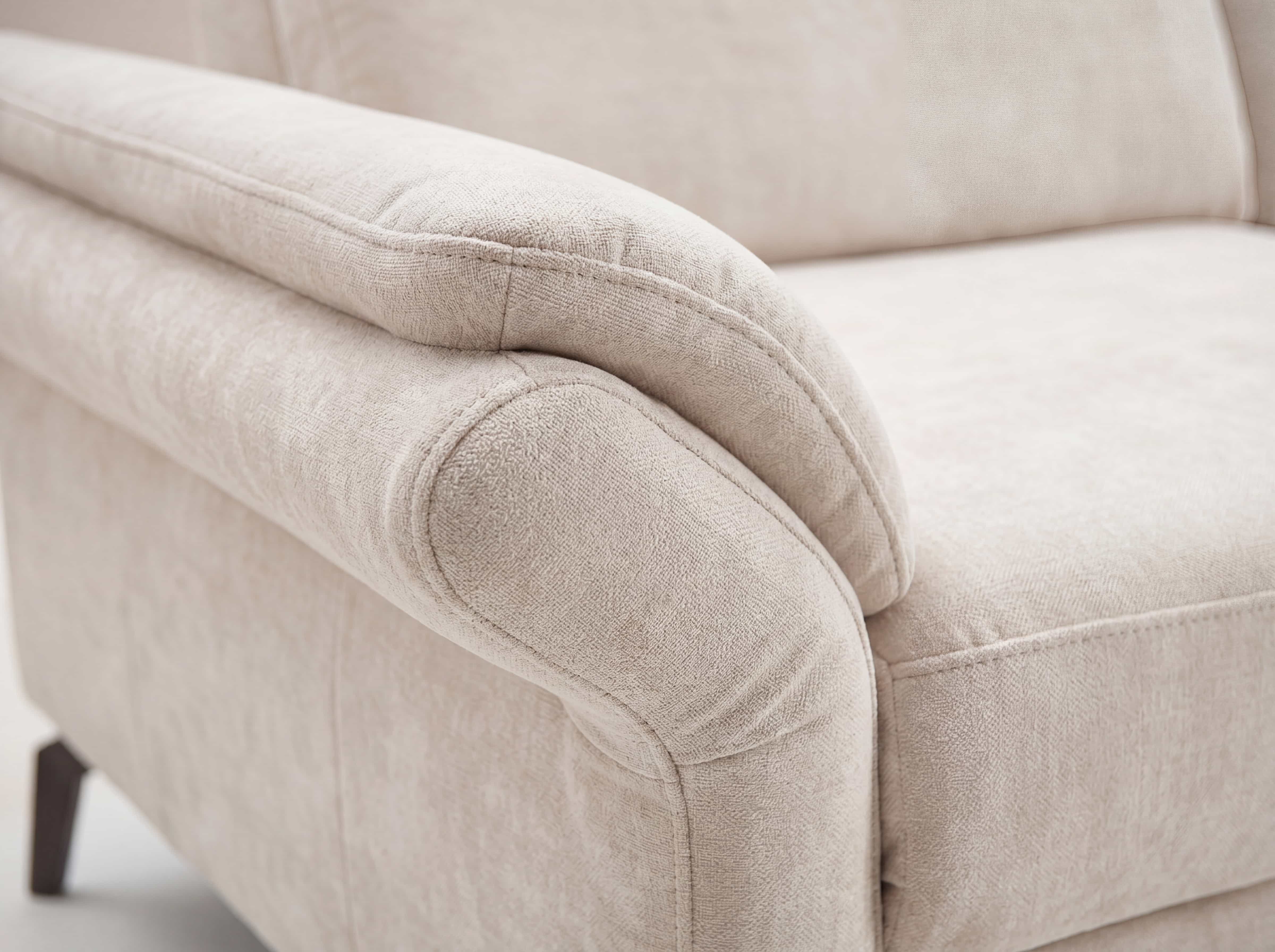 Sofa mit beigem Stoffbezug, gepolsterter Armlehne und sichtbarer Sitzfläche in Nahaufnahme
