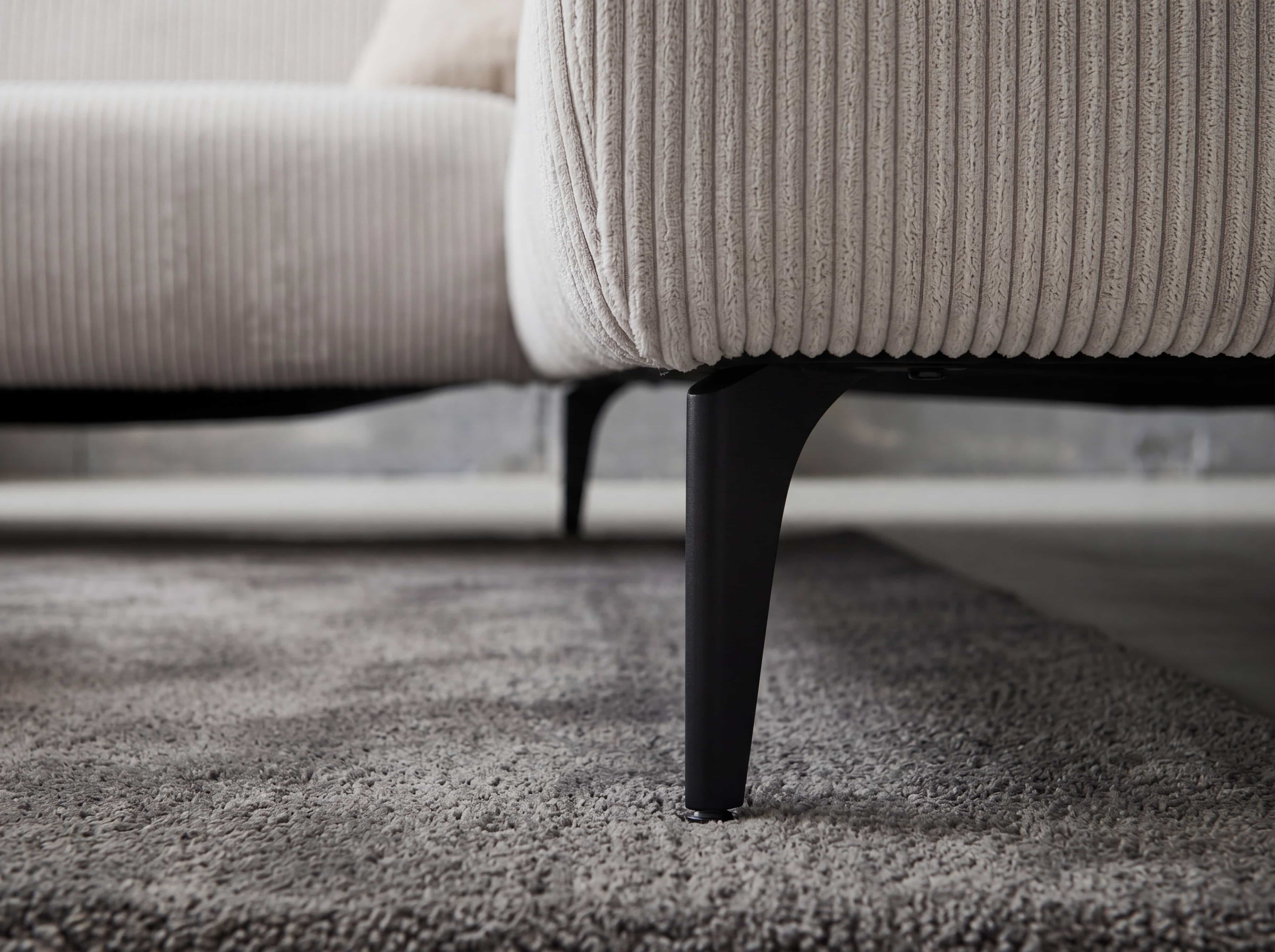 Ecksofa mit beigefarbenem Cordbezug und schwarzen, leicht ausgestellten Metallfüßen im Detail