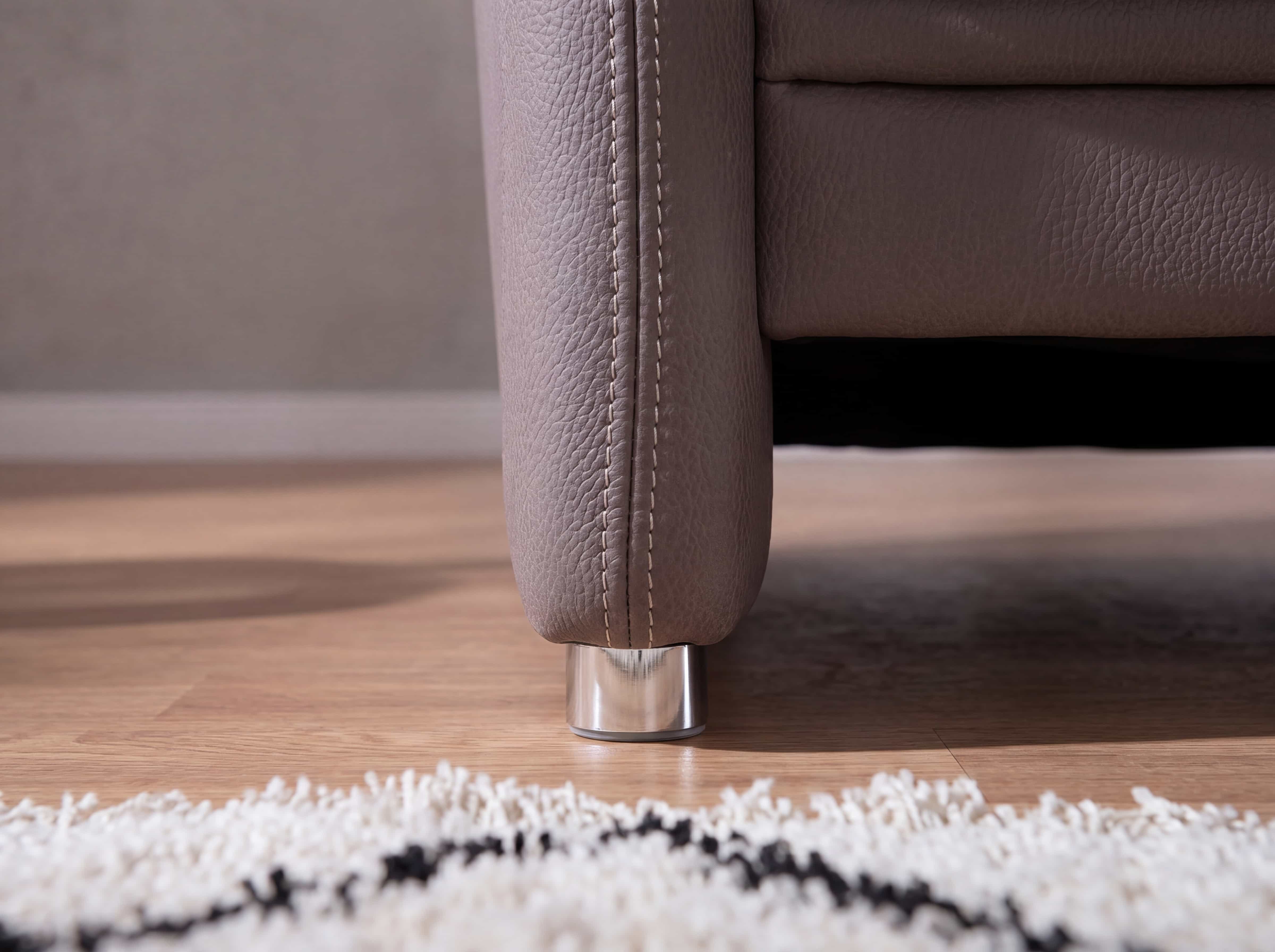 Nahaufnahme eines Sofafußes aus Metall mit beigefarbenem Lederbezug und sichtbarer Ziernaht
