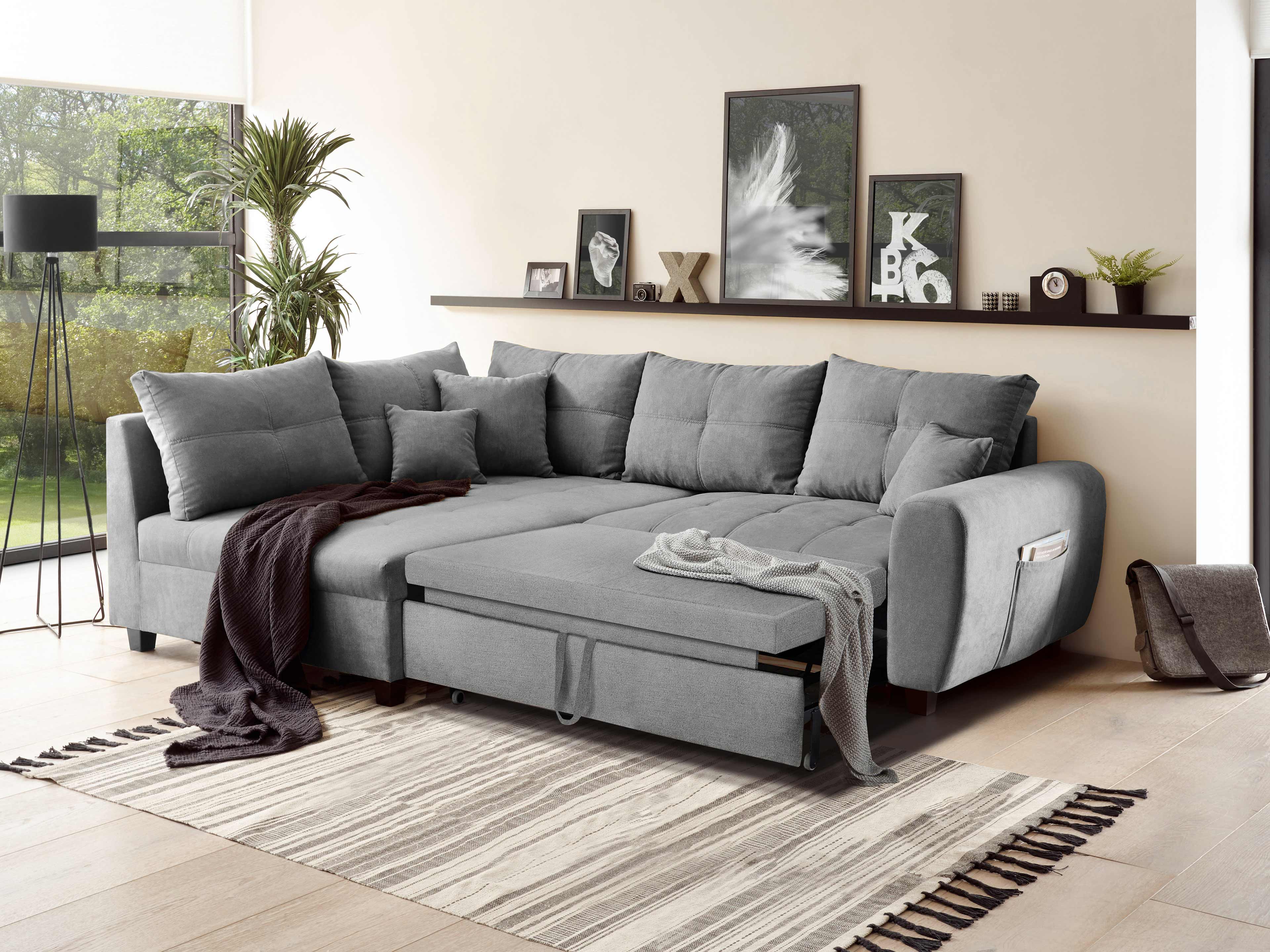Ecksofa Kabs Polsterwelt aus grauem Stoff mit Armlehnen, vielen Kissen und Schlaffunktion