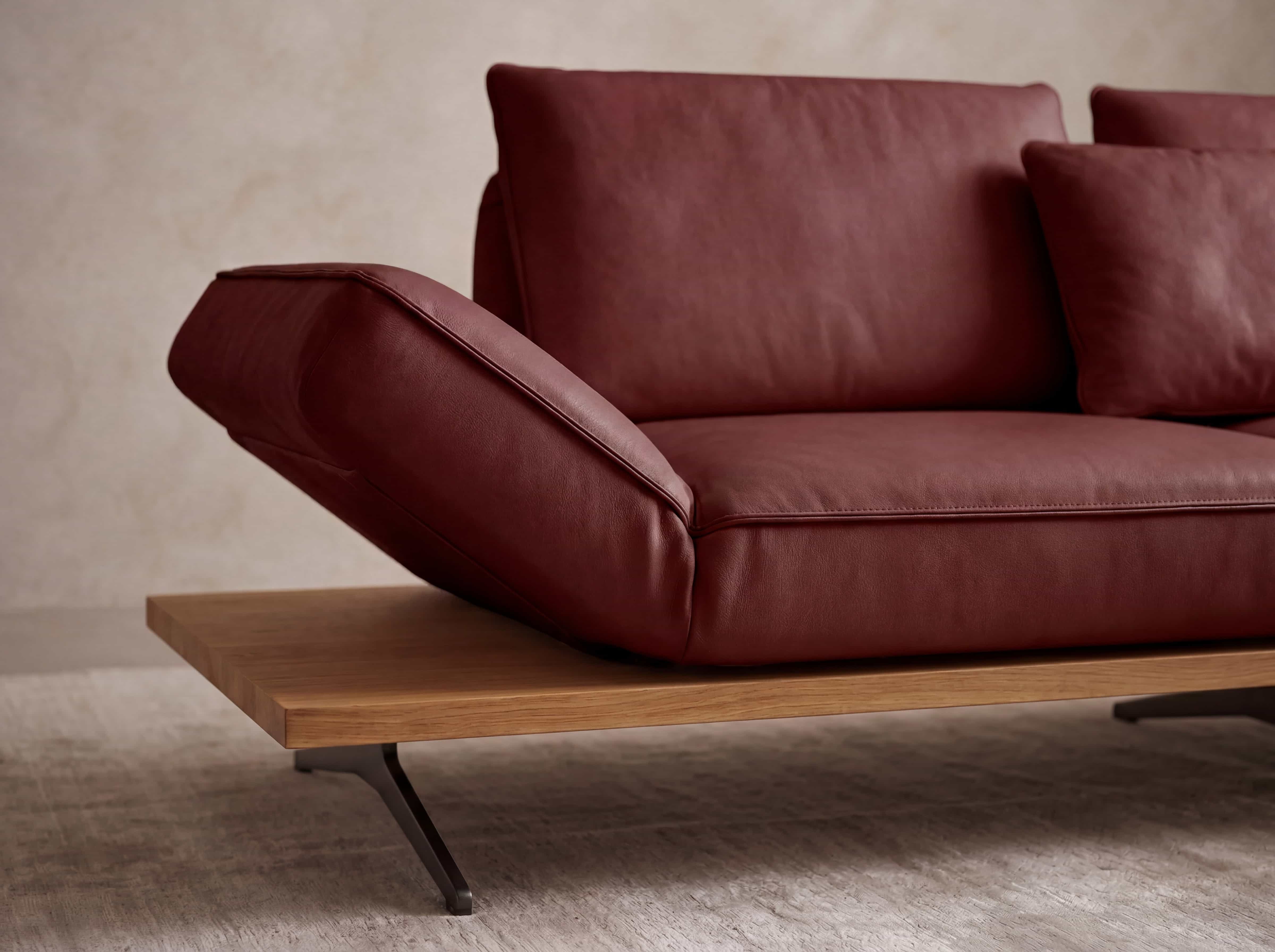 Ecksofa mit braunrotem Lederbezug, breiter Armlehne und Holzsockel mit Metallfüßen