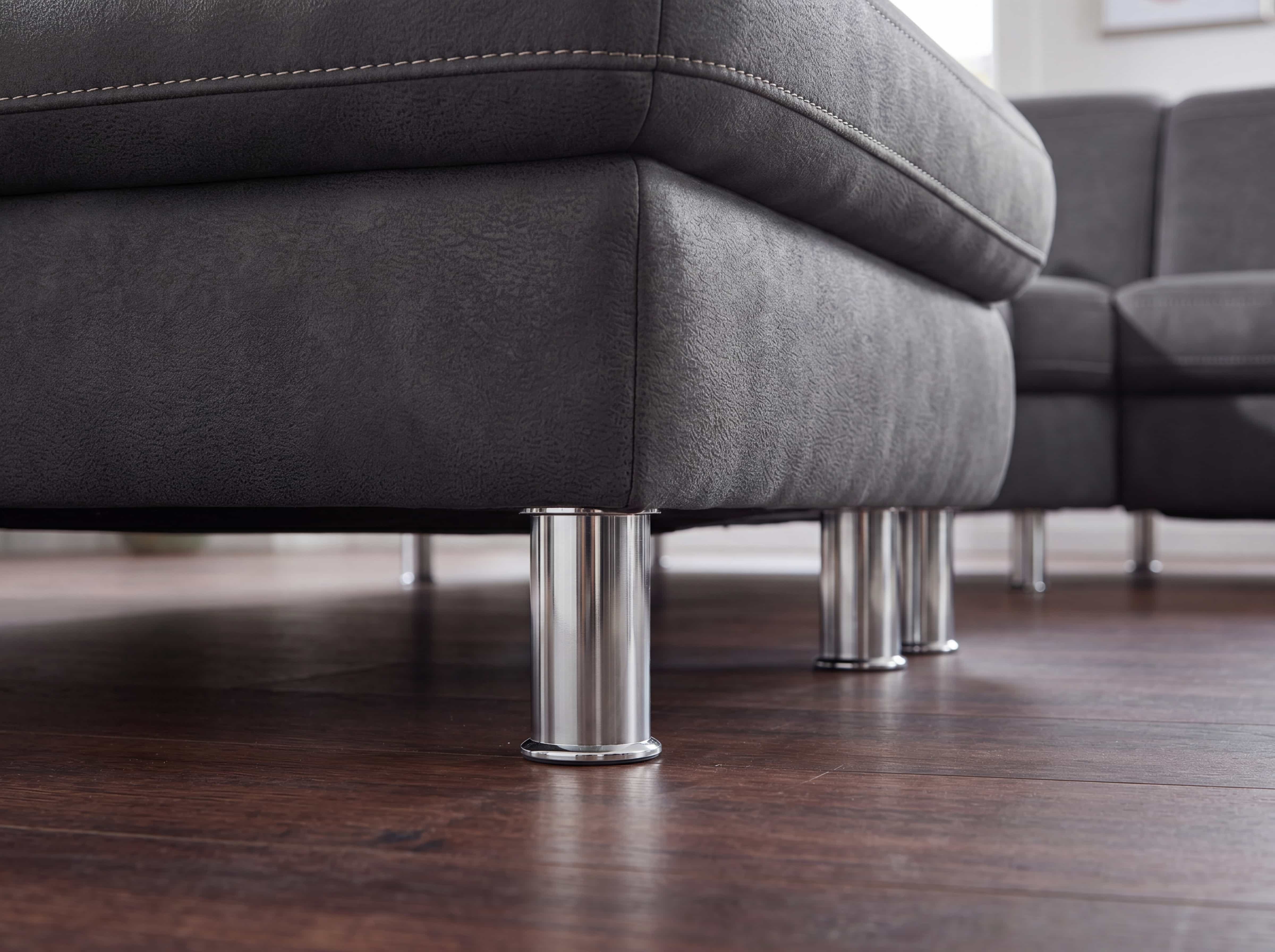Ecksofa mit grauem Stoffbezug, sichtbaren Ziernähten und zylindrischen Metallfüßen auf Holzfußboden