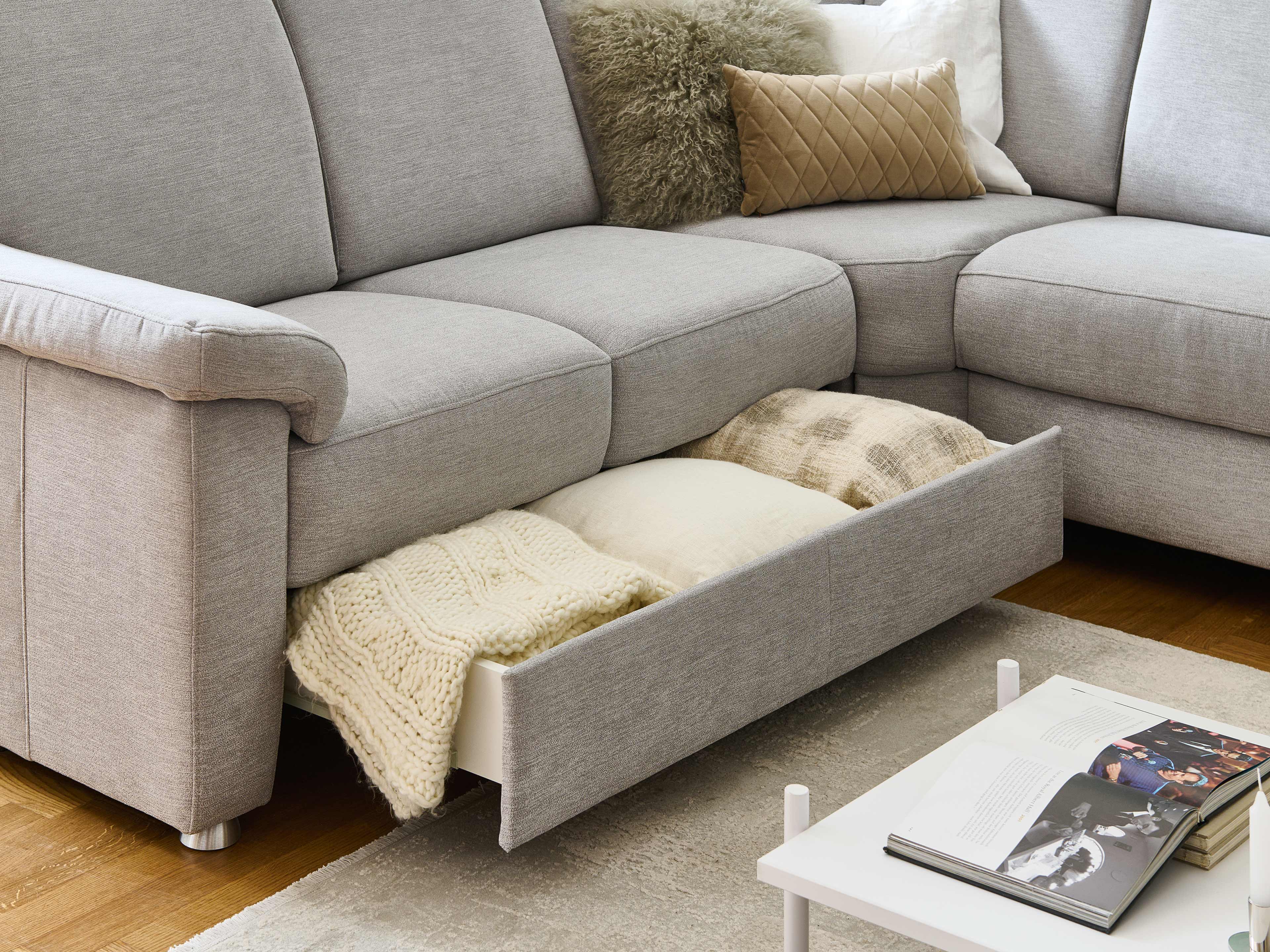 Ecksofa Modell mit hellgrauem Stoffbezug, Armlehnen und offenem Bettkasten mit Decken und Kissen