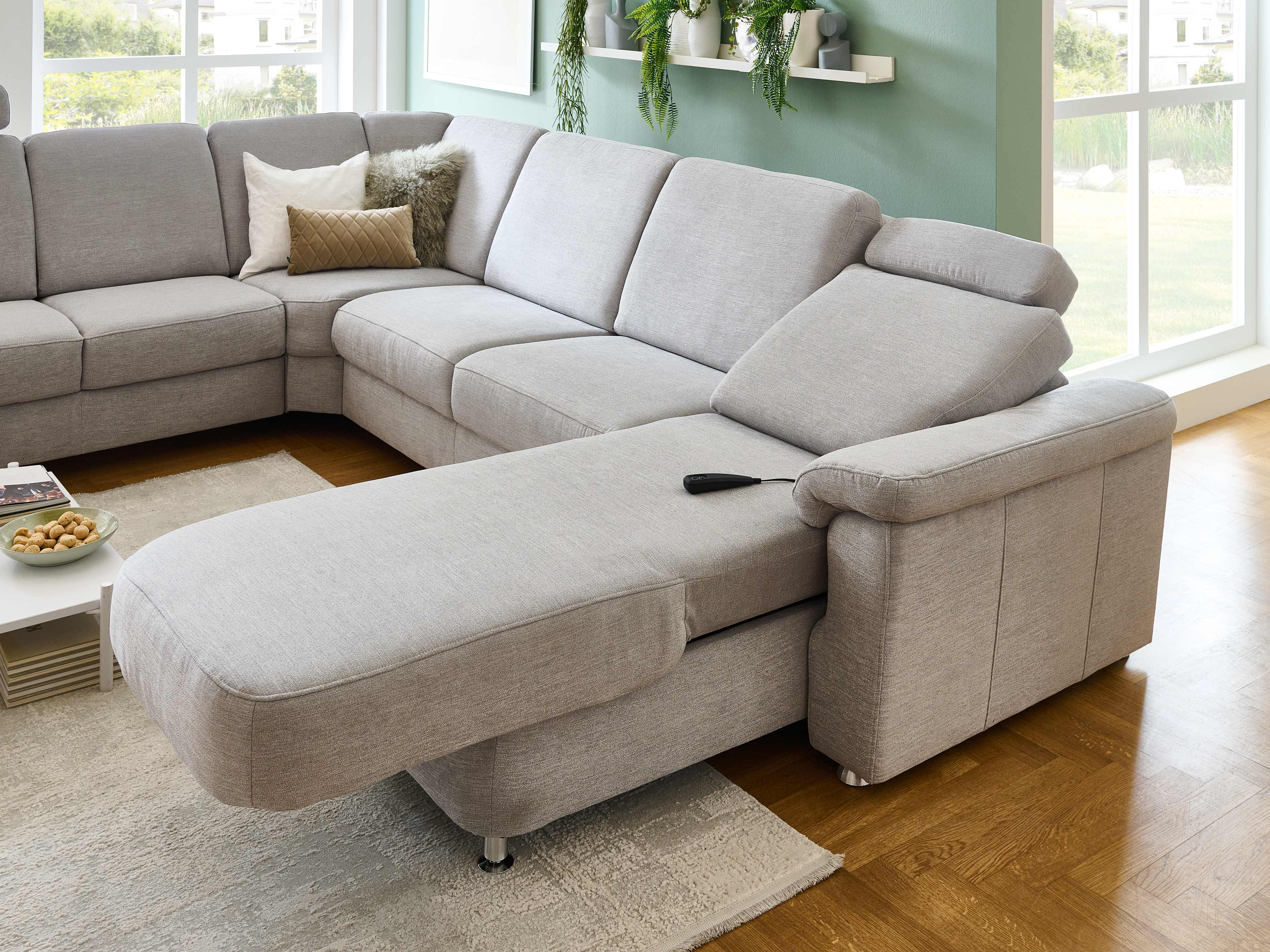 Ecksofa Kabs mit grauem Stoffbezug, gepolsterten Armlehnen und verstellbarer Kopfstütze
