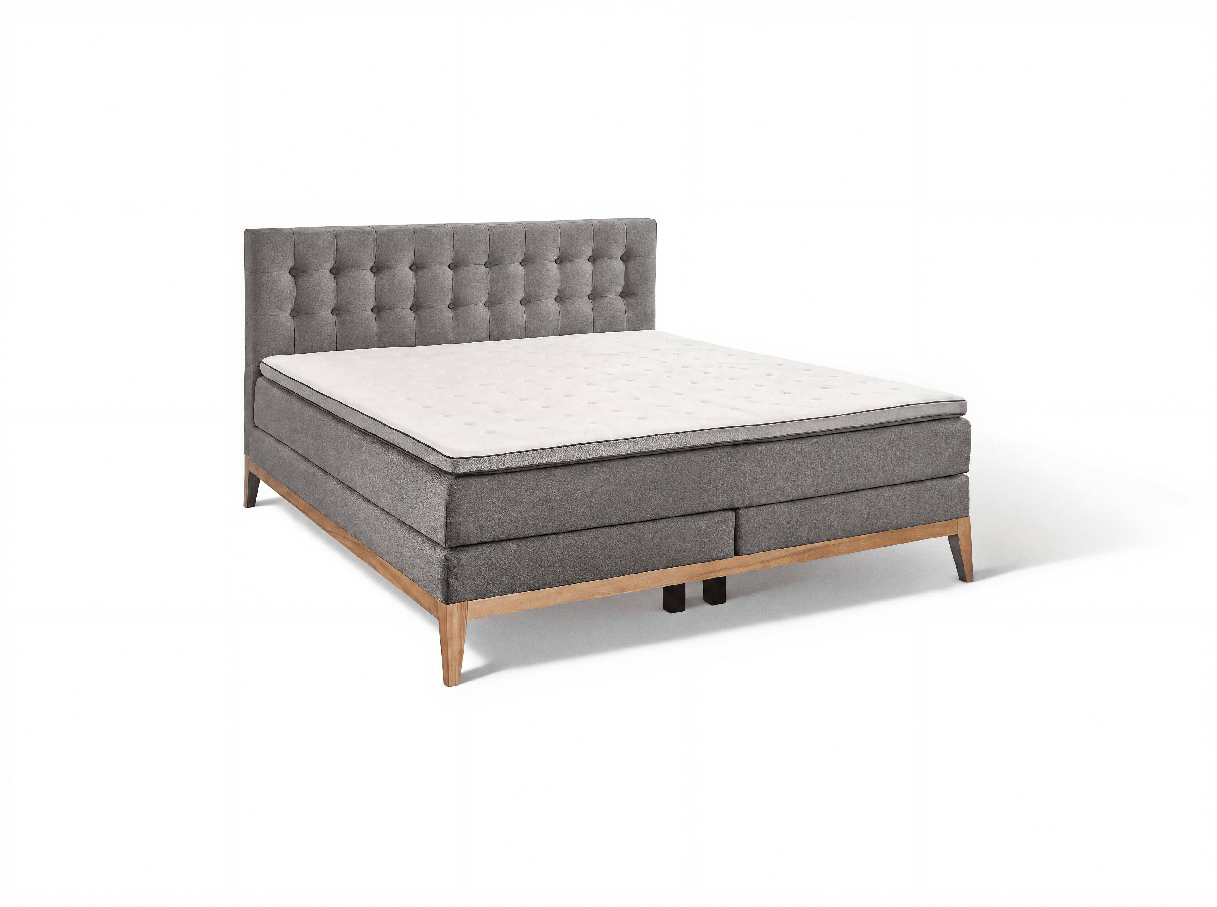 Boxspringbett mit grauem Stoffbezug, gepolstertem, gestepptem Kopfteil und Holzfüßen