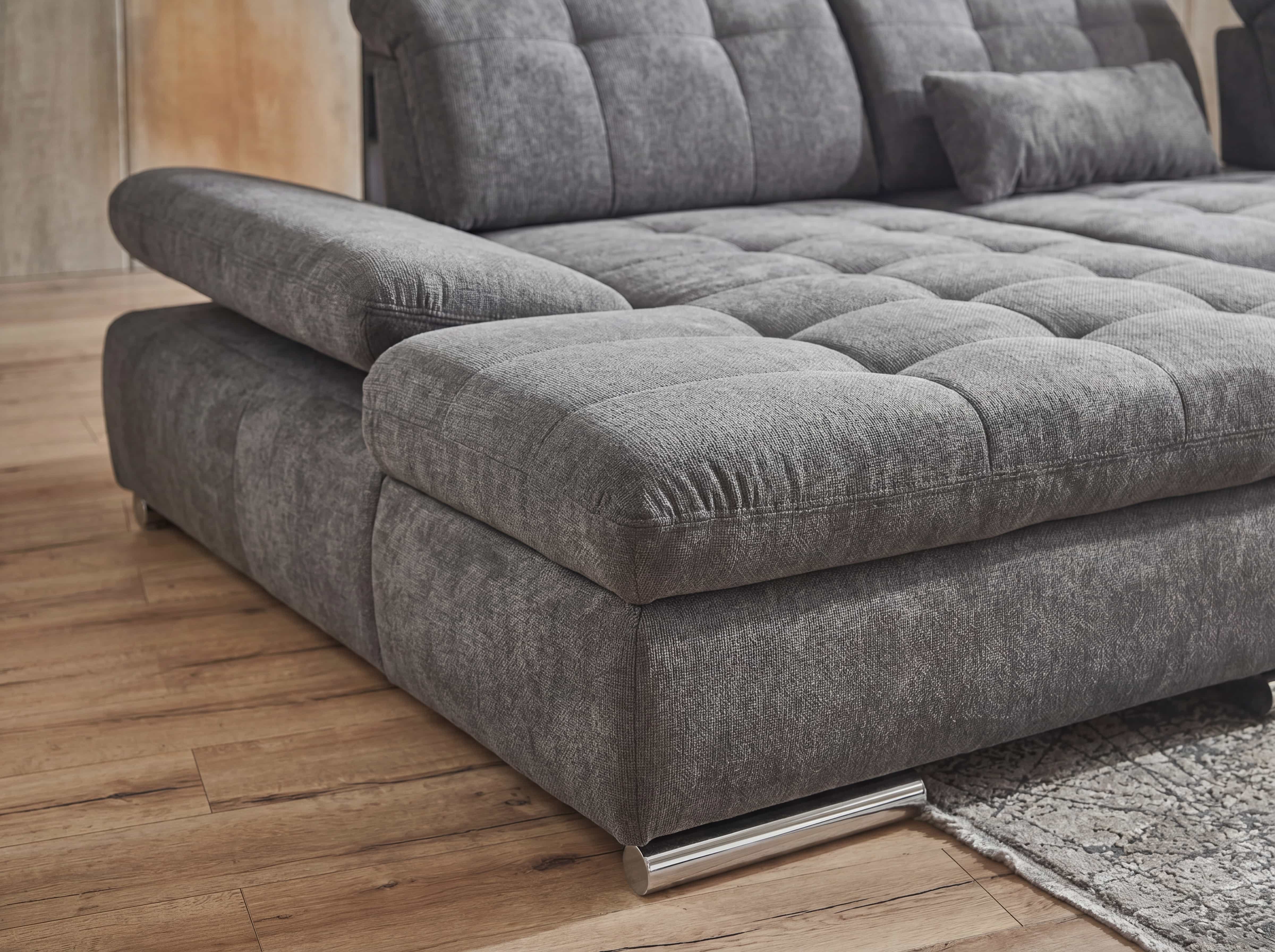 Ecksofa mit grauem Stoffbezug, breiter Armlehne, markanter Steppung und Metallfüßen