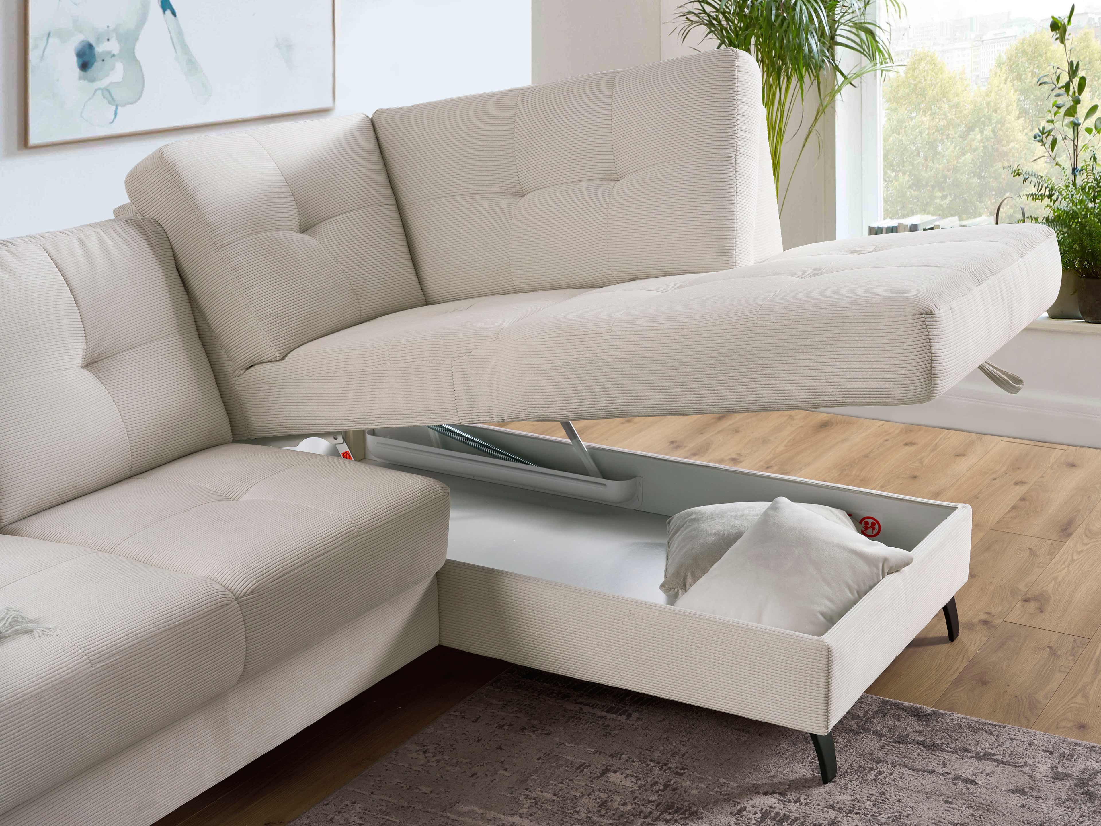 Ecksofa mit cremefarbenem Stoffbezug, sichtbarer Steppung, Bettkasten und schwarzen Metallfüßen