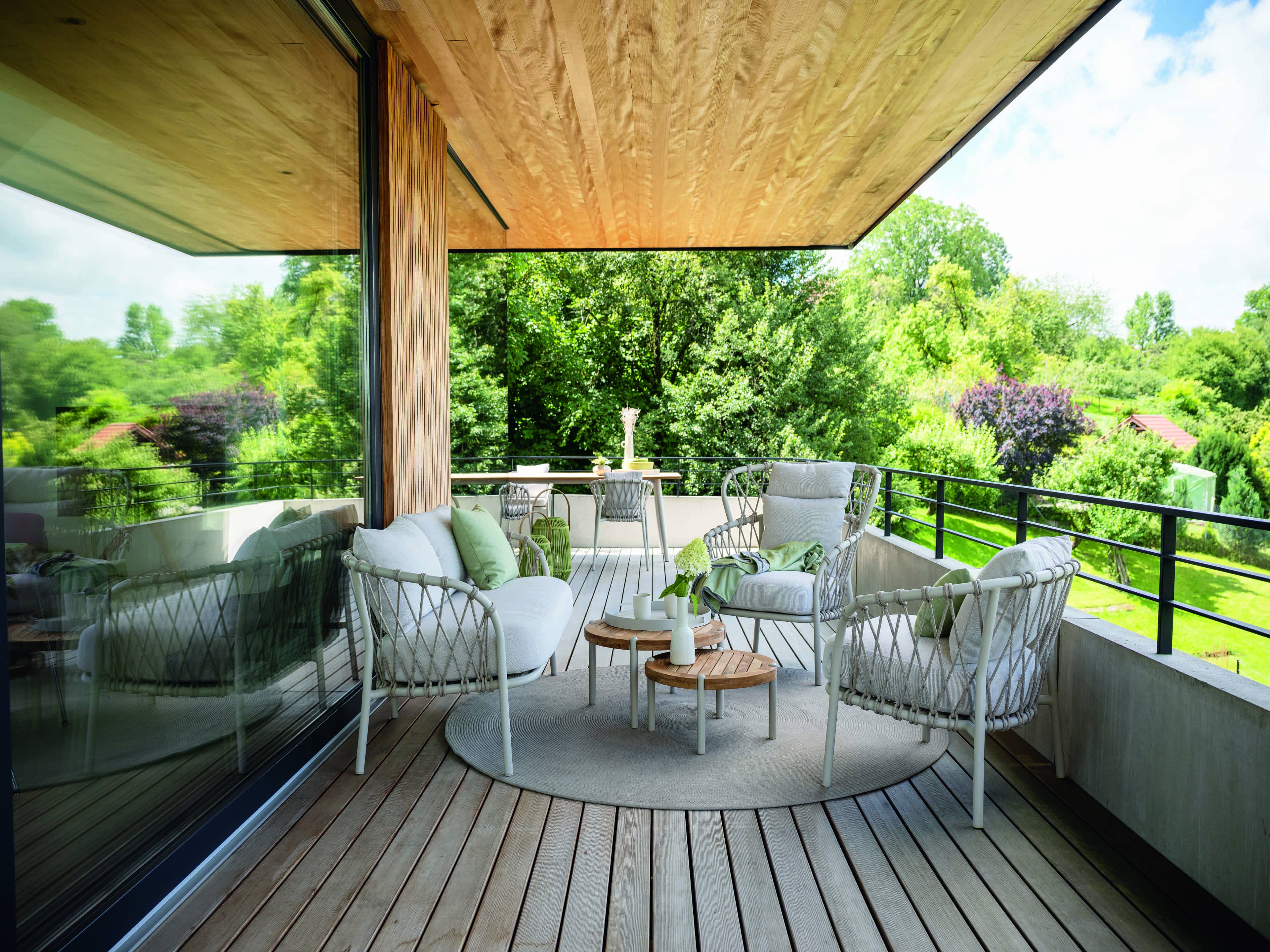 Gartenlounge mit weißen Polsterstühlen aus Geflecht und kleinem runden Holztisch auf Holzterrasse