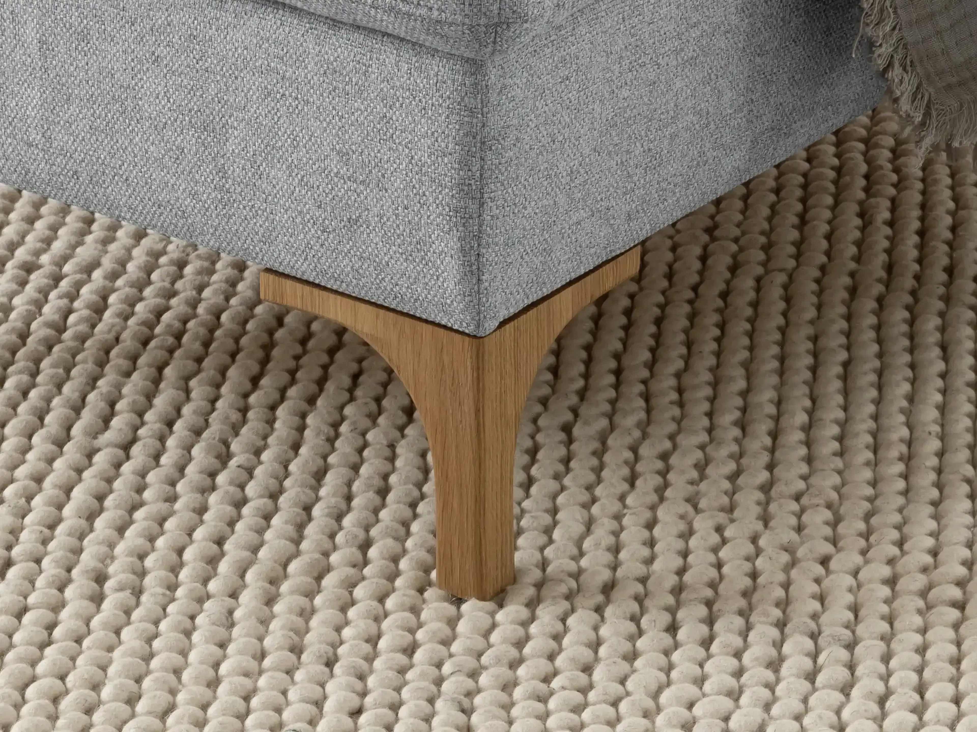 Boxspringbett mit hellgrauem Stoffbezug und eckigem Holzfuß auf strukturiertem Teppichboden