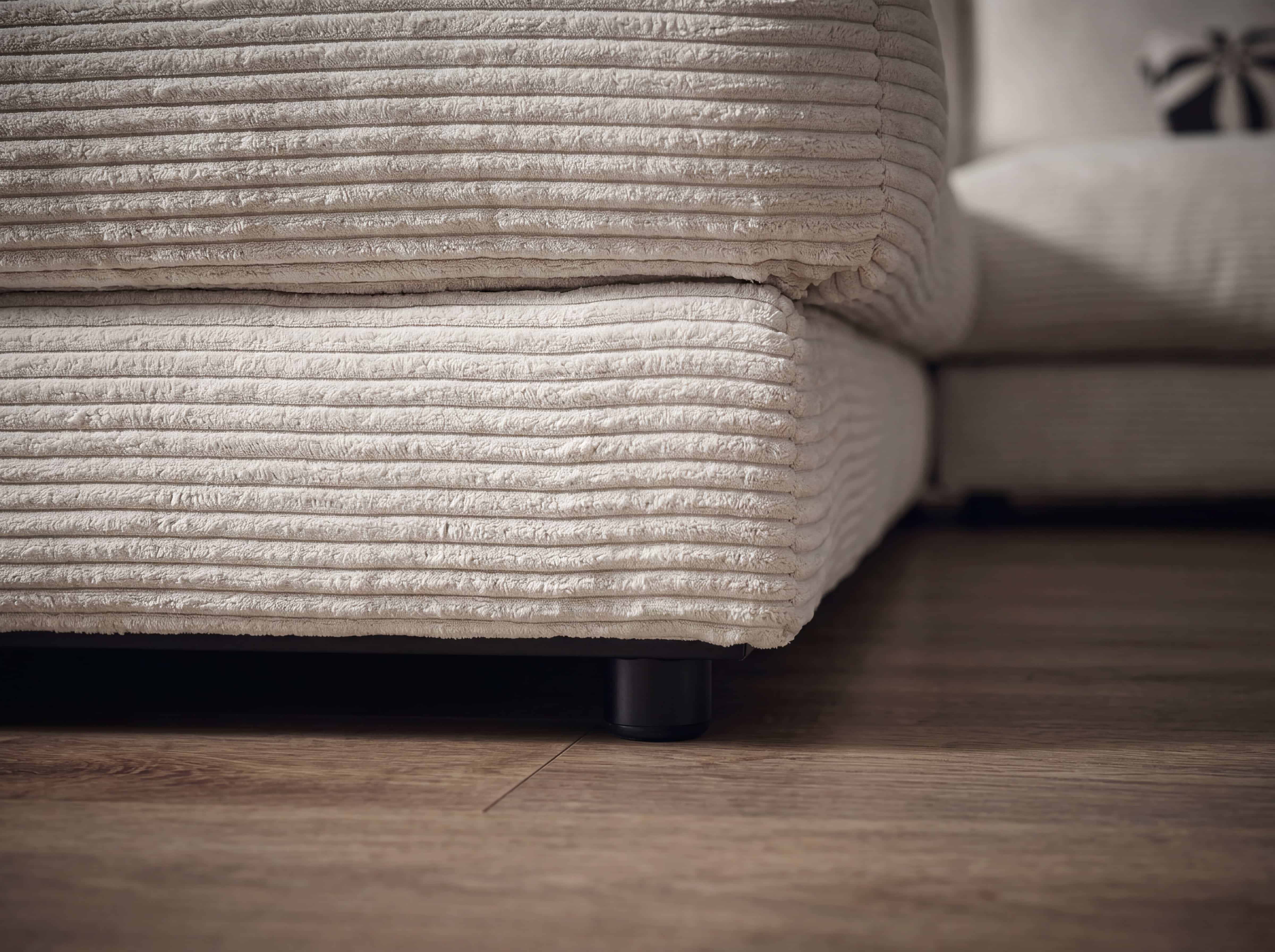 Ecksofa Kabs mit beigefarbenem Cordbezug, breiten Sitzflächen und schwarzem Rundfuß auf Holzboden
