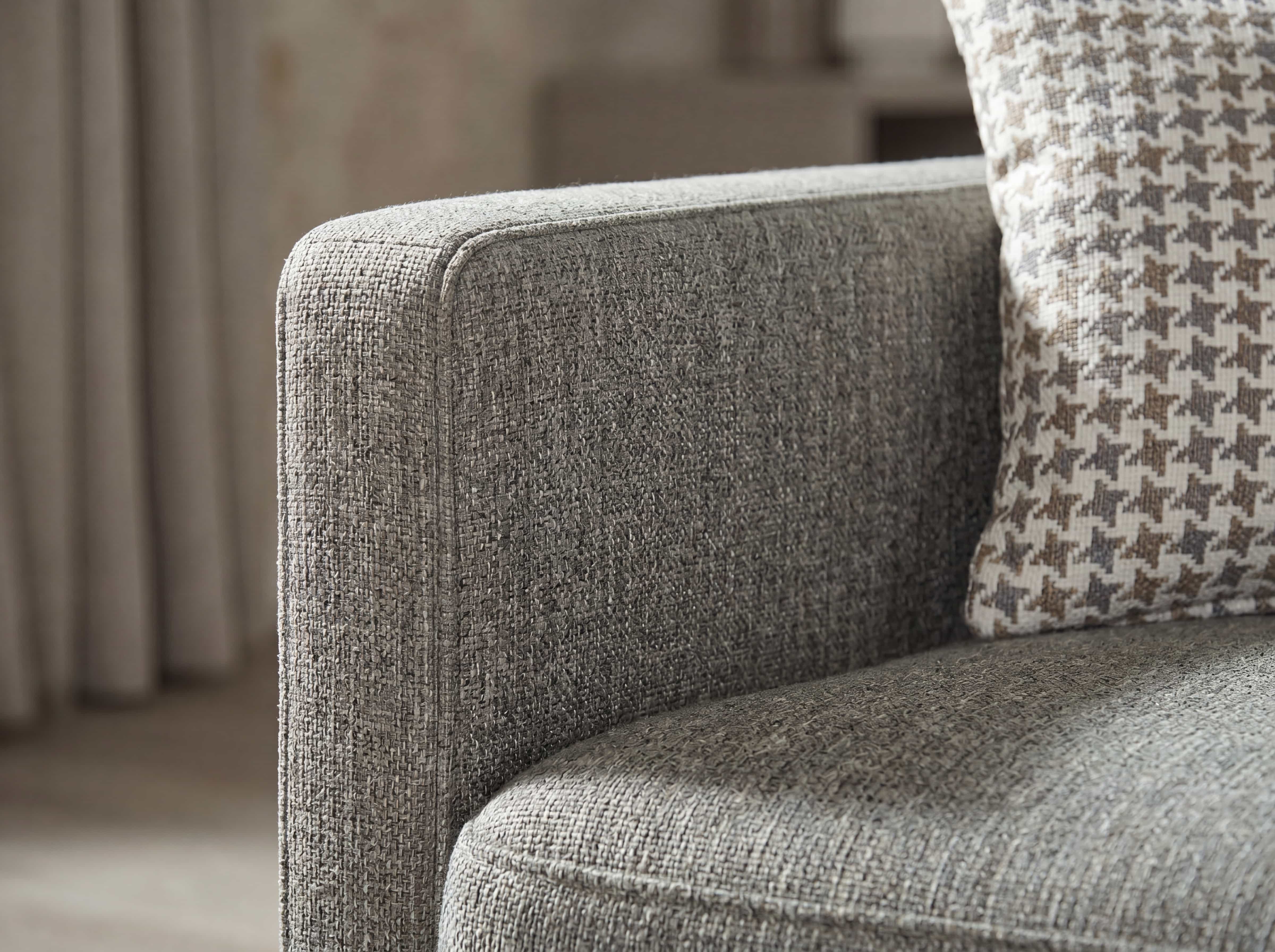 Ecksofa mit grauem Stoffbezug, gepolsterter Armlehne und Sitzfläche, Kissen mit Hahnentrittmuster