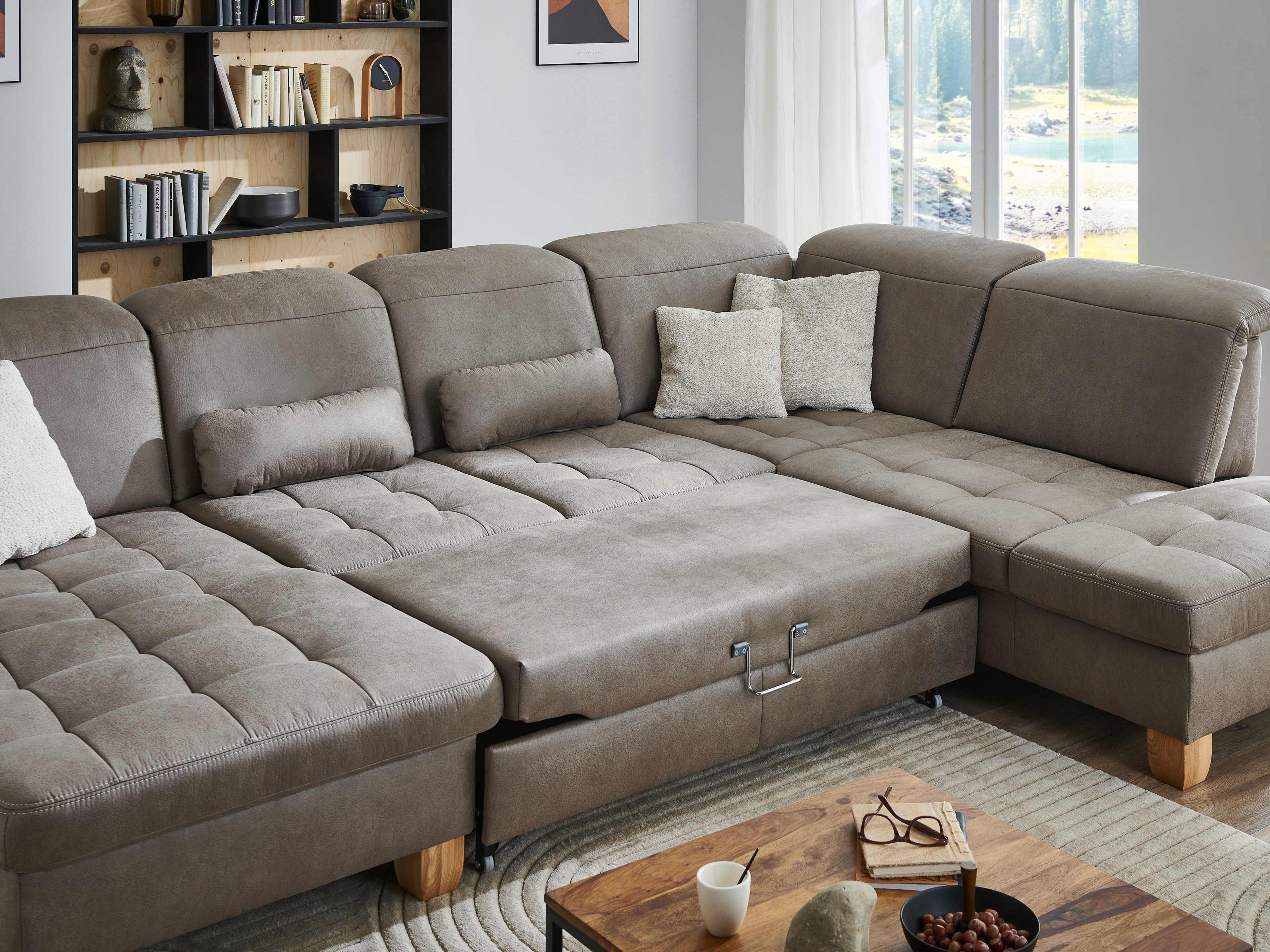 Ecksofa Livorno mit grauem Stoffbezug, gepolsterten Rückenlehnen und sichtbaren Holzfüßen