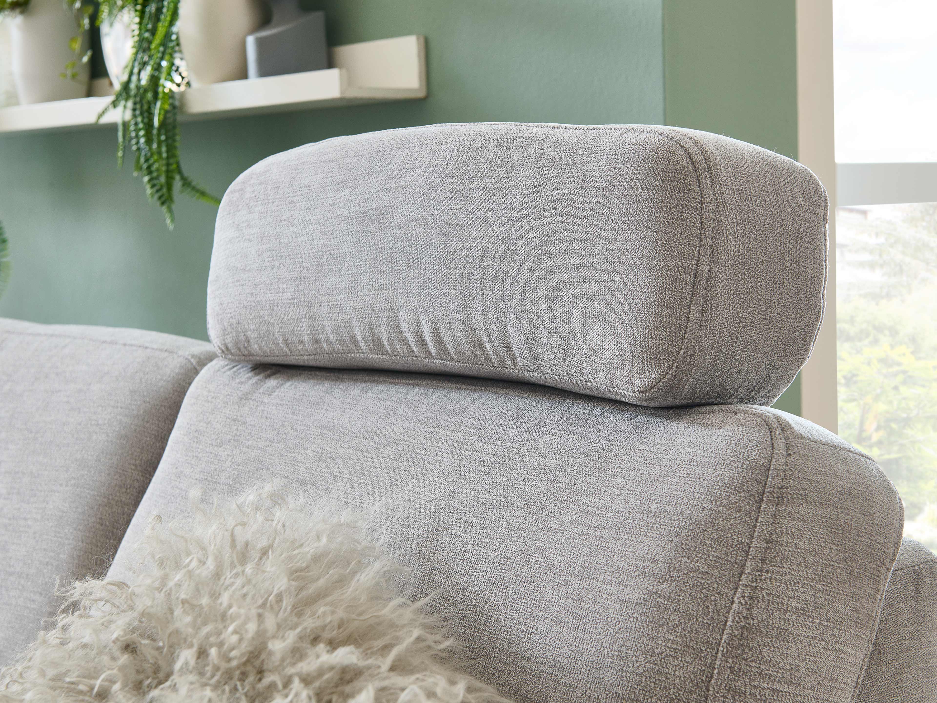 Kopfstütze eines grauen Stoffsofas mit strukturierter Oberfläche, Fokus auf Polsterung und Nahtdetails