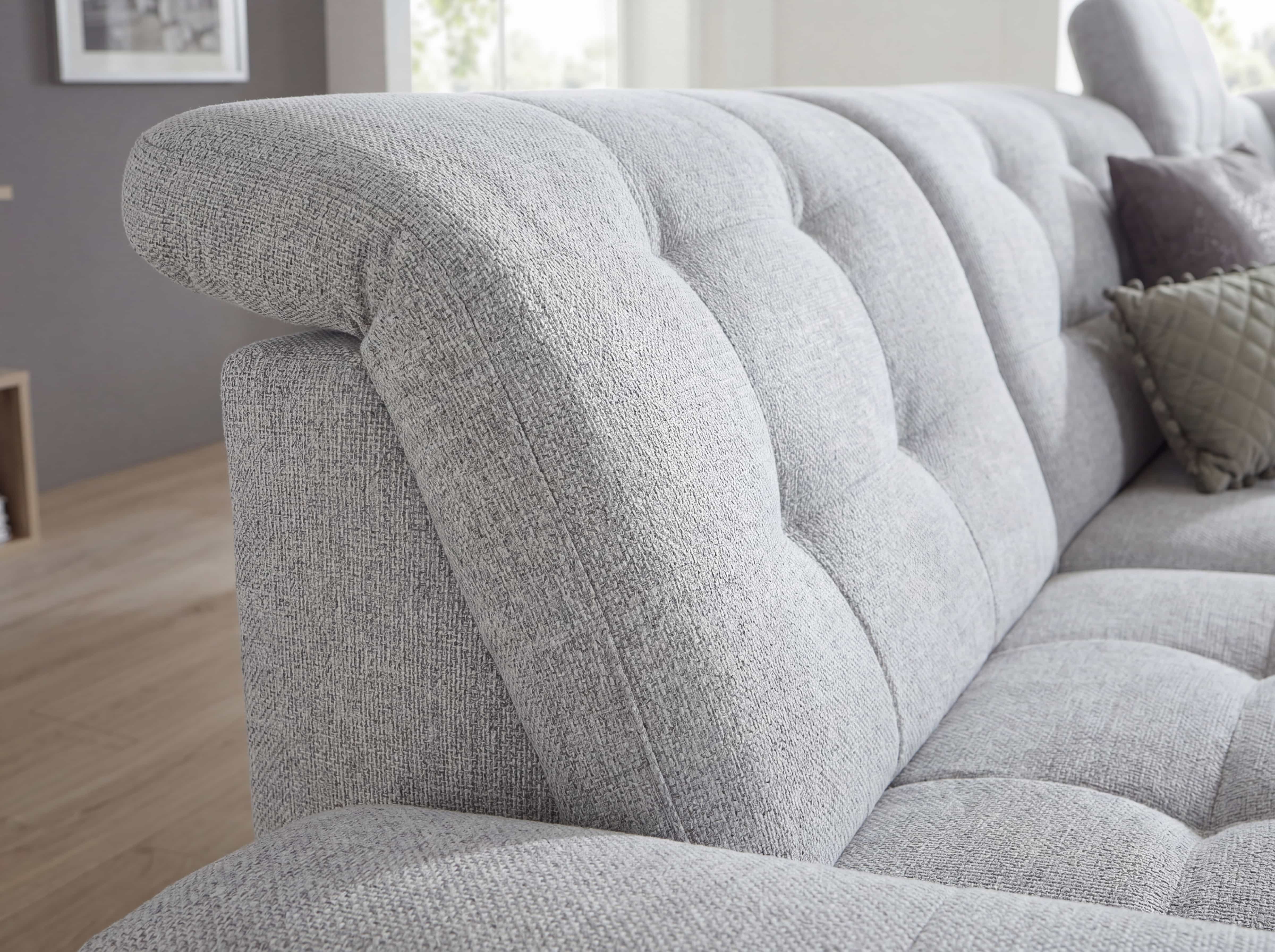 Ecksofa mit grauem Stoffbezug, gestepptem Polster und abgerundeter Armlehne in Nahaufnahme