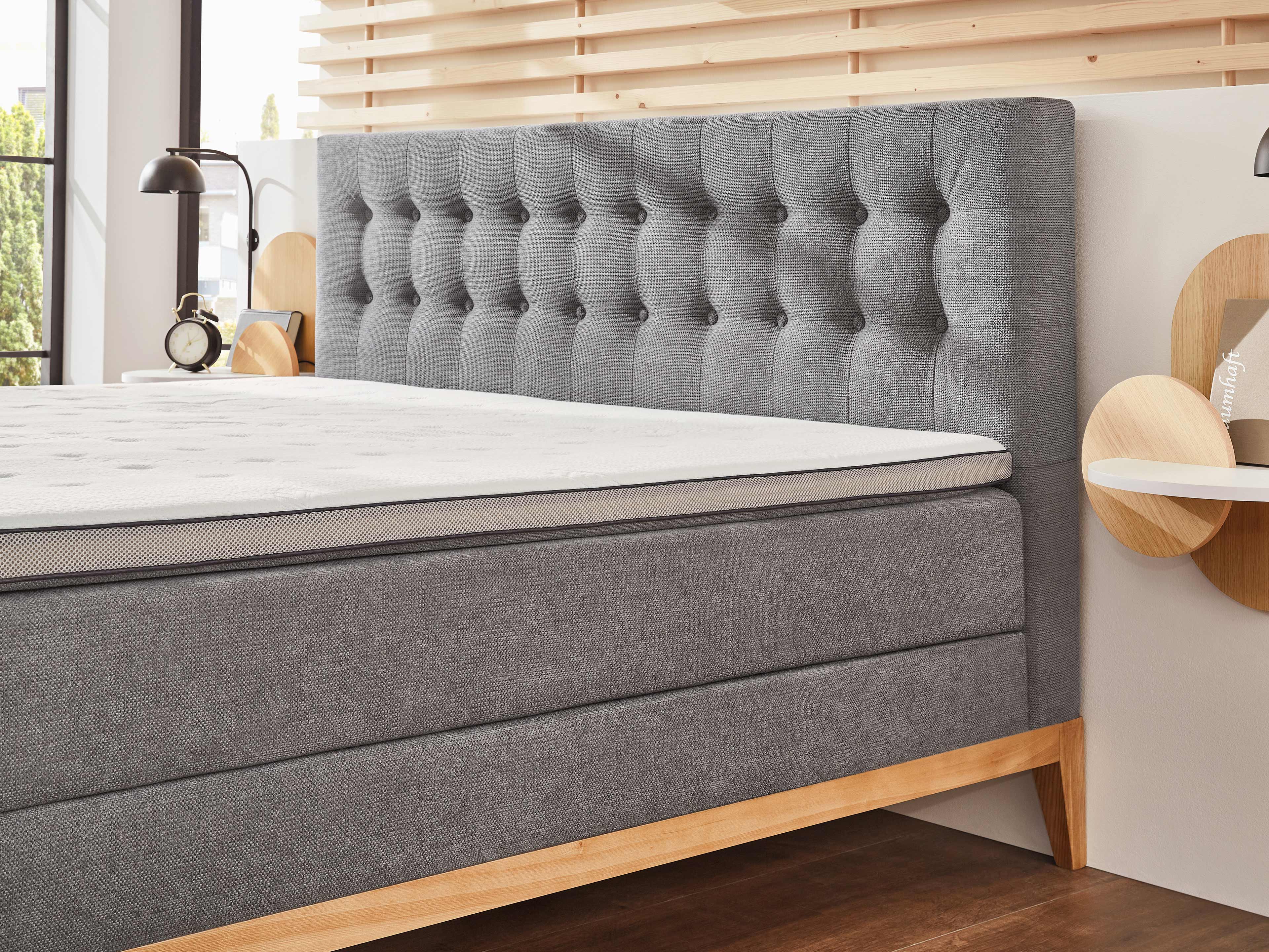 Boxspringbett mit grauem, strukturiertem Stoffbezug, gepolstertem Kopfteil und Holzfüßen