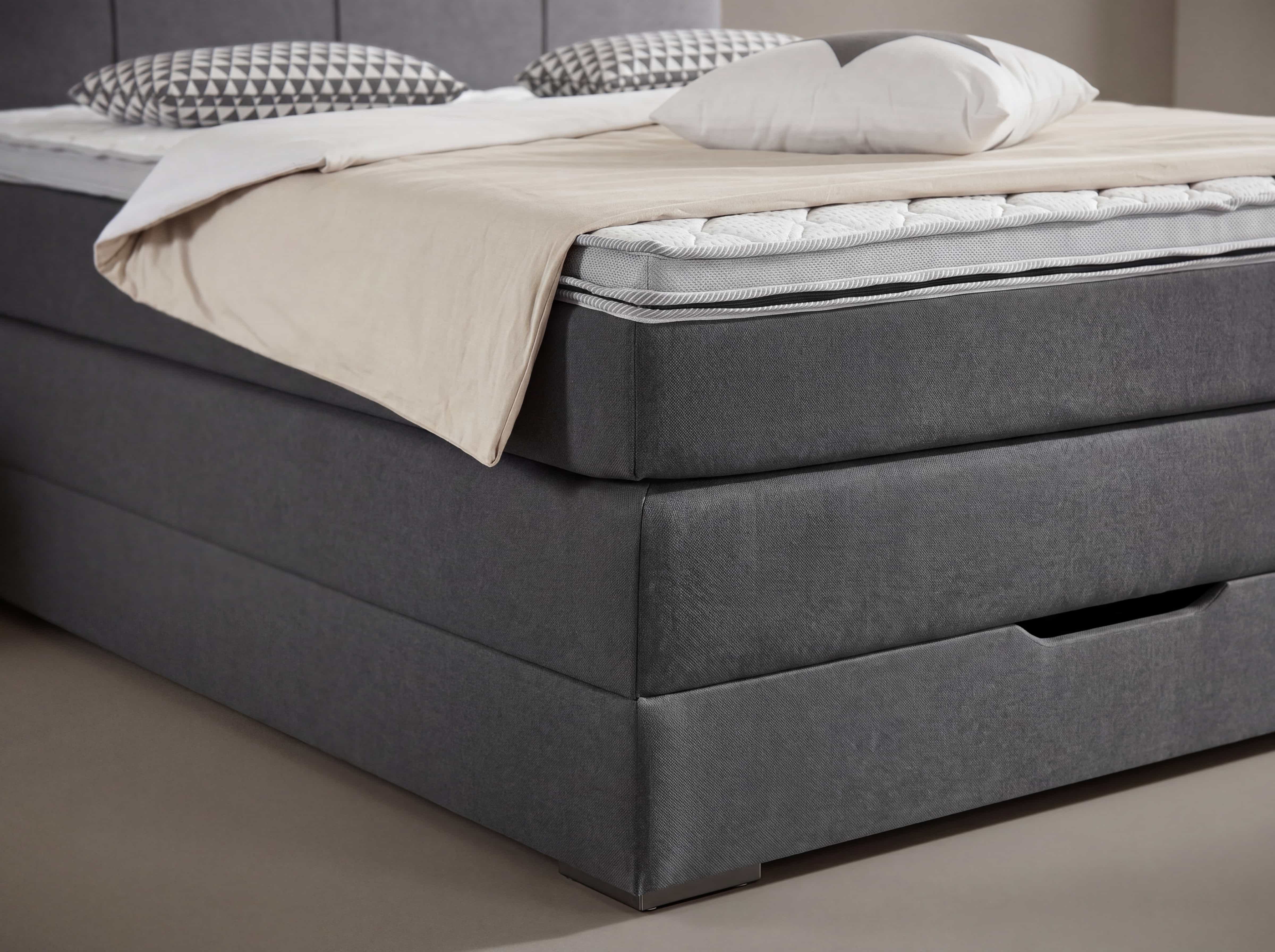 Boxspringbett mit grauem Stoffbezug, gepolsterter Unterbox und sichtbarer Matratze in Nahaufnahme