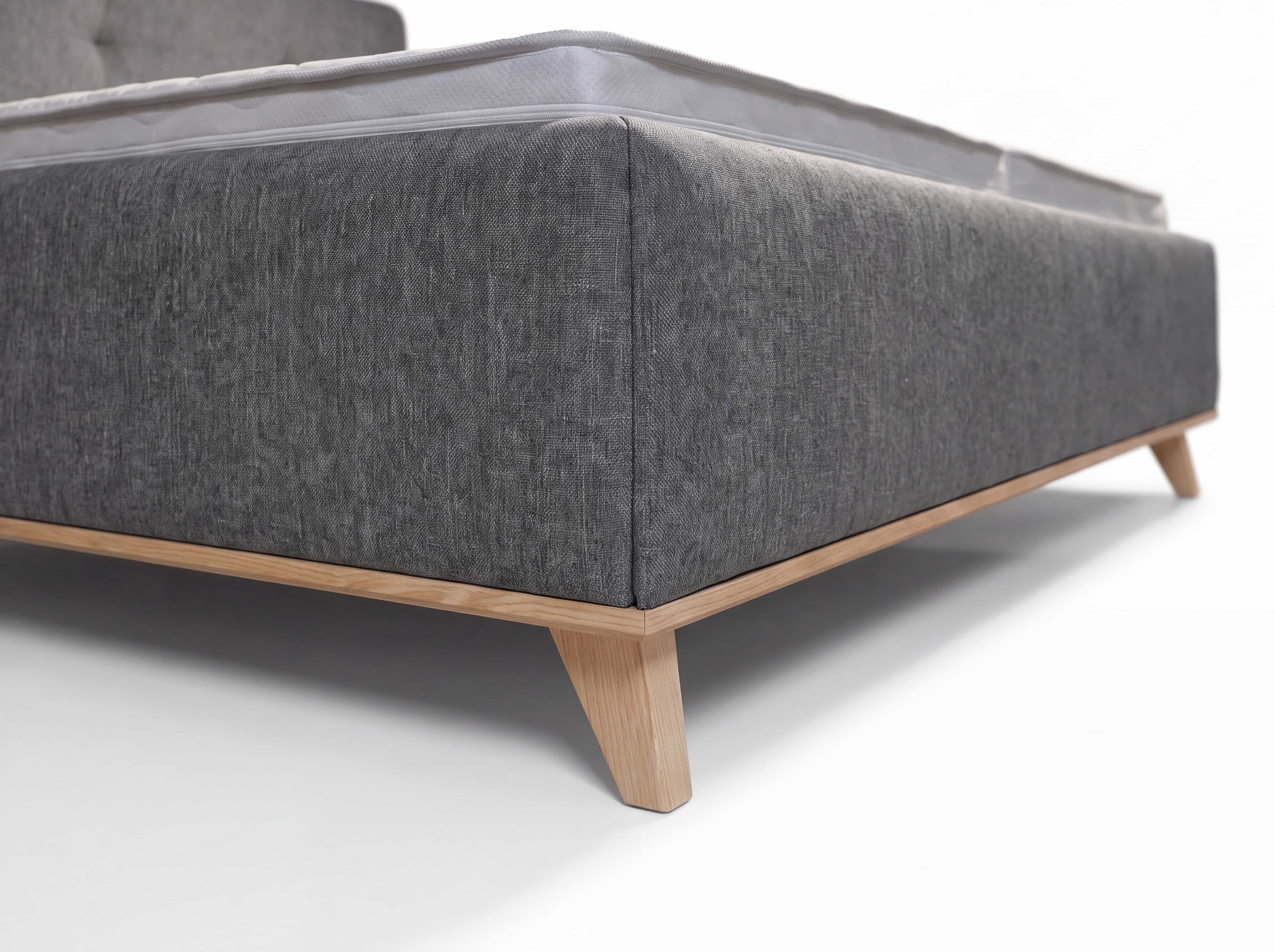 Polsterbett mit grauem Stoffbezug, hellem Holzgestell und eckigen Füßen, Detailansicht Ecke