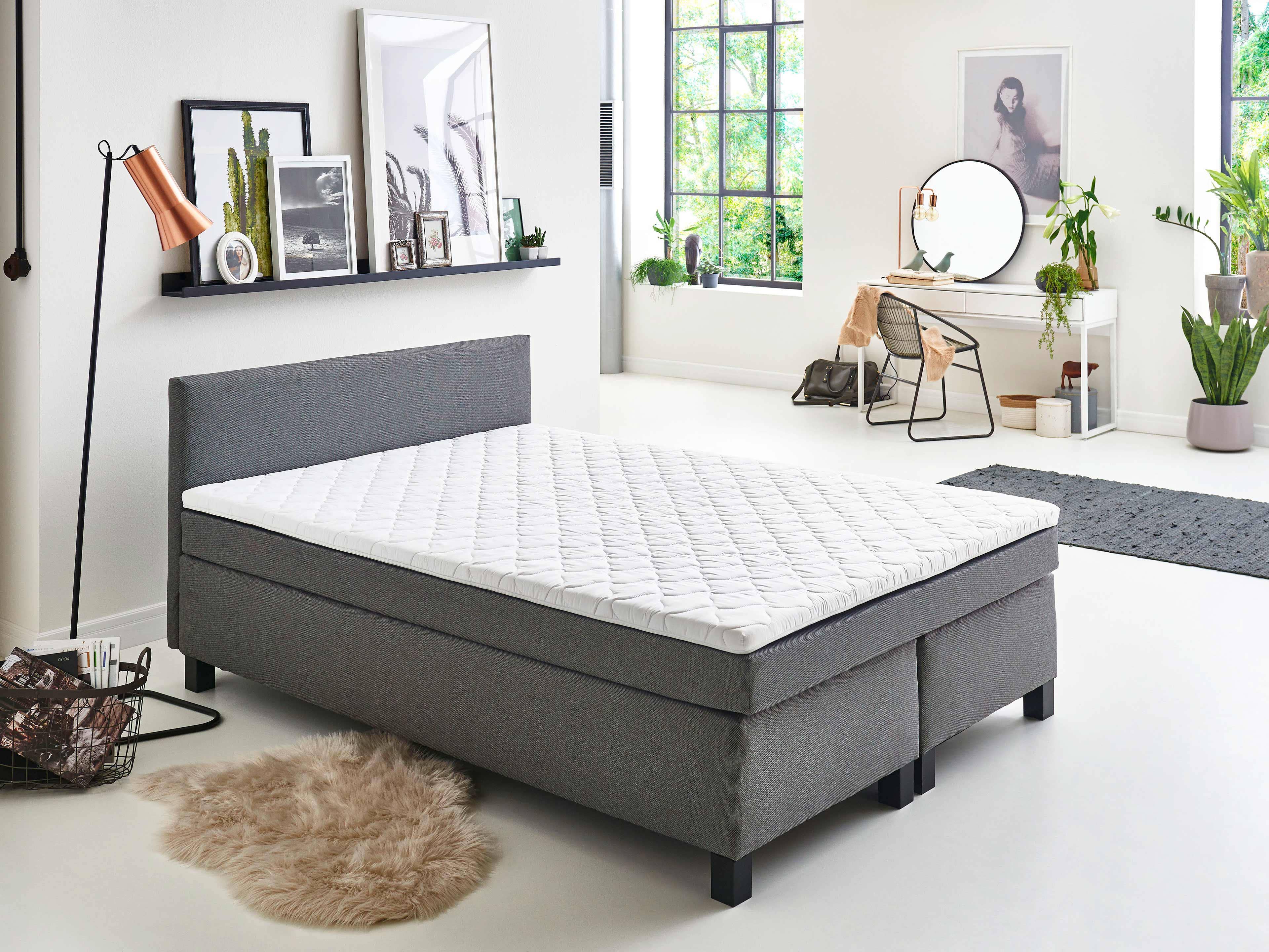 Boxspringbett mit grauem Stoffbezug, geradem Kopfteil und schwarzen Bettfüßen in Frontansicht