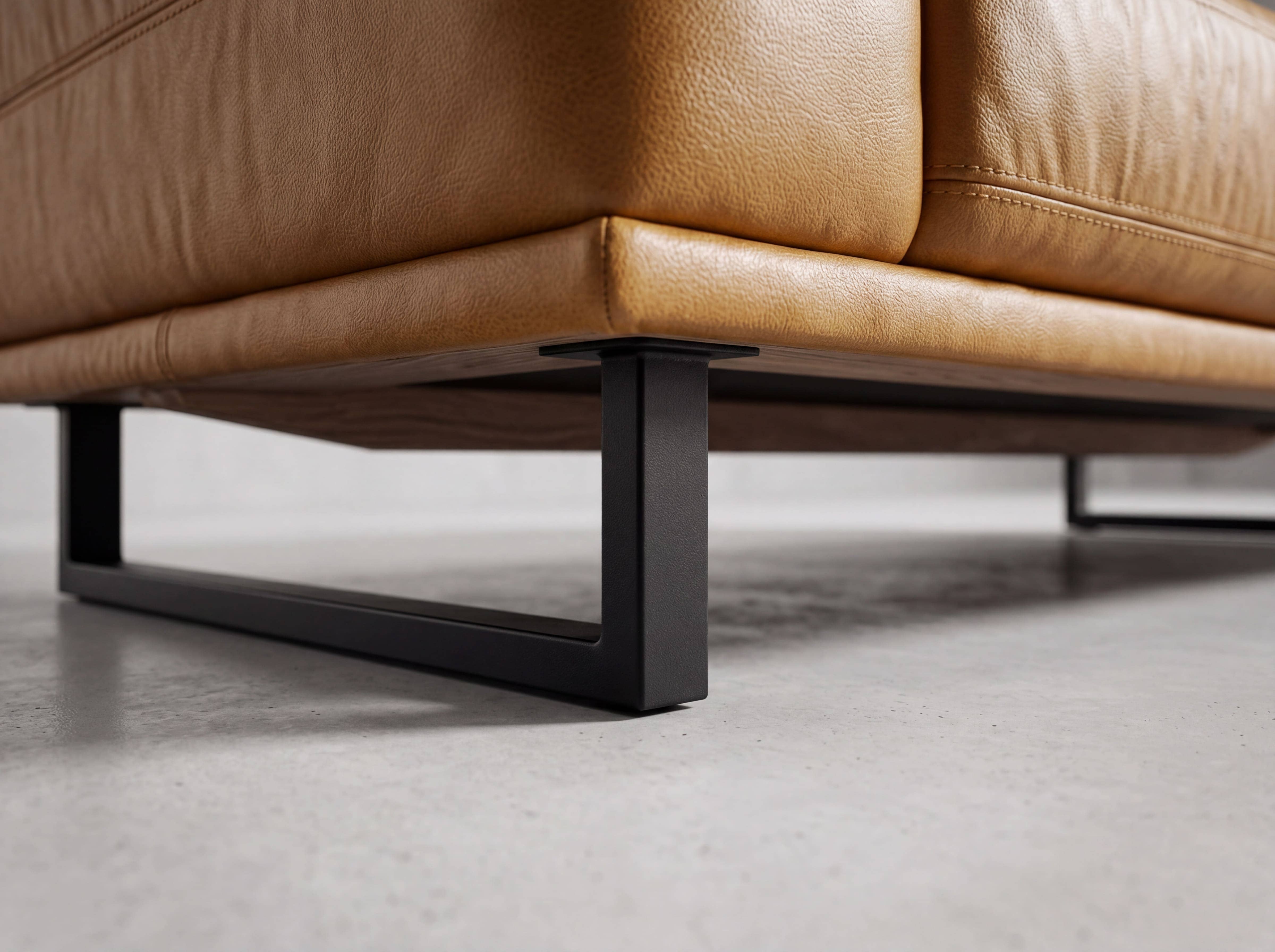 Detailansicht eines Sofafußes aus schwarzem Metall unter einem cognacfarbenen Ledersofa