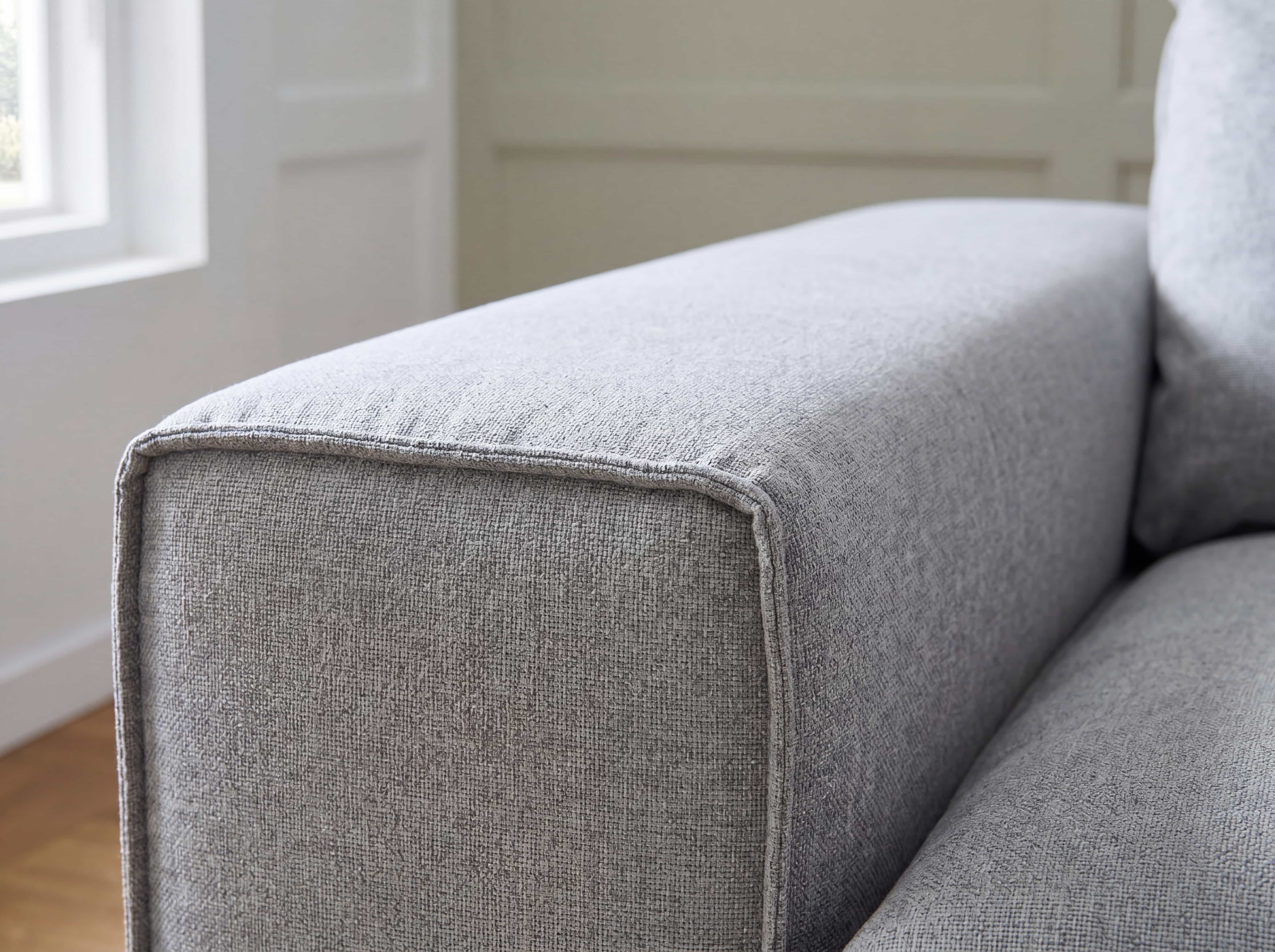Graues Sofa mit rechteckiger Armlehne und sichtbarer Struktur im Stoffbezug aus Nahaufnahme